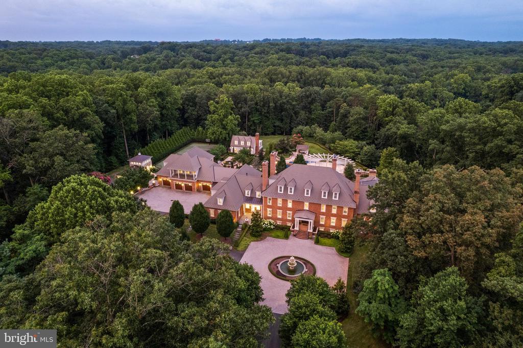 Welcome to Edgehill Estate—an extraordinary residence that embodies timeless elegance and modern luxury in the heart of Oakton. Set on 11 beautifully landscaped acres, this stately, oversize brick and stone colonial—inspired by the historic Carter’s Grove—offers over 20,000 square feet of meticulously designed living space. This grand residence masterfully blends classic American Colonial design with the highest level of modern luxury, technology, and artisan detail. Every inch reflects unparalleled craftsmanship—from hand-carved Chesney mantels imported from London to walls hand-painted by famed Hollywood designer Harold Grieve. A formal foyer sets the tone with coffered ceilings, a foot of crown molding, custom millwork, plaster medallions, mahogany inlays, and antique wall sconces, guiding you into the heart of the home. The Primary Suite is a wing of its own, featuring dual dressing rooms, a sitting room with coffee bar, a spa-inspired marble bath with a steam shower, a fireplace, and balcony access overlooking the grounds. Designed for both everyday comfort and extraordinary entertaining, the estate includes a chef’s kitchen with Thermador appliances; multiple living rooms, a library, a home gym, a steam room, a sauna, a jetted hot tub spa room, and access to one of the largest residential pools in Fairfax County with grotto waterfall, fire bowls, infitity edge, and slide.The resort-style grounds offer travertine throughout, pergolas, an alfresco outdoor kitchen, a tennis court, multiple fire features, and a three-tiered fountain, surrounded by lush landscaping that blooms year-round. A 13-car garage complex, guest house, elevators, and commercial-grade generator ensure the highest level of comfort, privacy, and preparedness.Edgehill Estate is more than a home—it’s a legacy property offering an unmatched lifestyle of privacy, prestige, and timeless beauty.