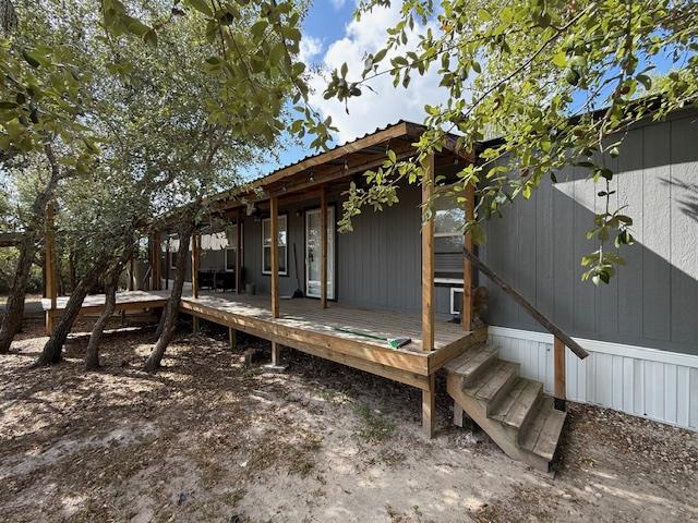 Exterior view of a wooden deck and entrance of a home in Rockport, Texas, surrounded by trees and natural landscaping, showcasing a cozy, inviting atmosphere for potential buyers.