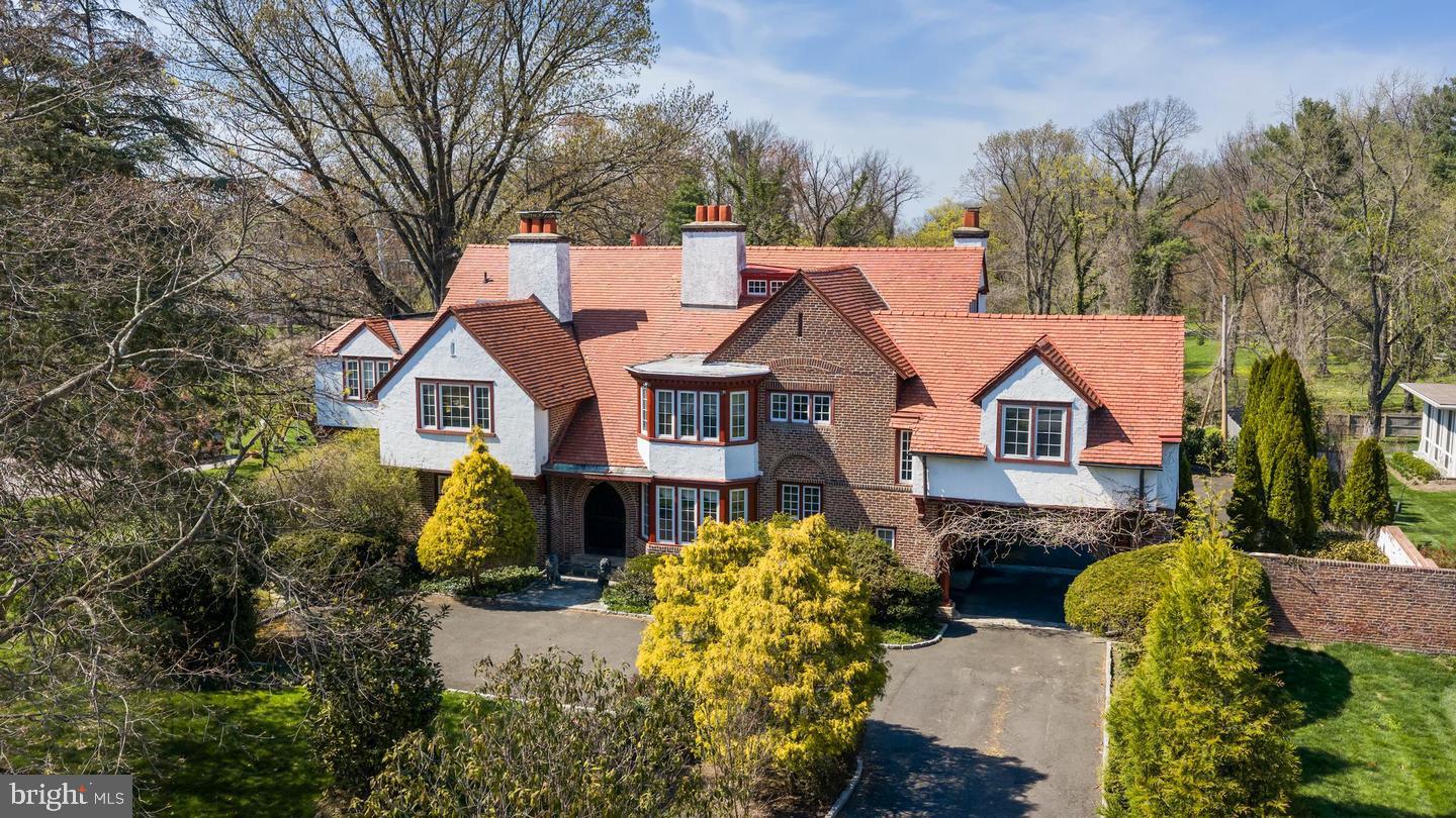 Classic residence with a striking combination of brick and stucco, steeply pitched rooflines, and distinctive chimneys, set amidst mature landscaping and lush grounds. A beautifully crafted arched wood entry door with divided-light glass panels and rich natural finishes creates a memorable sense of arrival.Inside, a grand foyer introduces the home’s scale and architectural detail, with a fireplace serving as a focal point upon entry. To the left, a series of elegant living spaces unfolds, including a formal sitting room with fireplace and double French doors that open to a side patio, filling the room with natural light. Straight ahead, the formal dining room is anchored by its own fireplace and adjoins a sunlit sitting area with French doors leading to the rear patio, creating a seamless indoor-outdoor connection.The butler’s pantry connects both the foyer and dining room and leads to the lower level. The kitchen is well-appointed with a large center island, DCS cooktop, double Wolf ovens, Sub-Zero refrigerator, and custom cabinetry. Adjacent to the kitchen, a casual dining and sitting area with fireplace opens to another patio through French doors, and provides access to the garage and additional storage. A powder room is discreetly located off the foyer beneath the main staircase.Upstairs, the second level unfolds along a central hall, offering both privacy and flexibility. Just off the main hallway, a separate corridor creates a distinct bedroom wing, with two bedrooms, a full bath, and access to the third level all thoughtfully arranged off this space. An additional bedroom with its own full bath is positioned nearby, providing flexibility for guests or extended use. One of the secondary rooms features a fireplace, adding warmth and character.A sitting area along the main hall offers a quiet retreat, while a private office is set at the end of the corridor. The primary suite is thoughtfully situated for privacy and includes its own fireplace and a spacious bath with a large soaking tub, creating a comfortable and secluded retreat.The third level extends the living space further, offering a sitting area, full bath, expansive recreation or playroom, and an additional bedroom—well suited for guests, work, or flexible living arrangements.