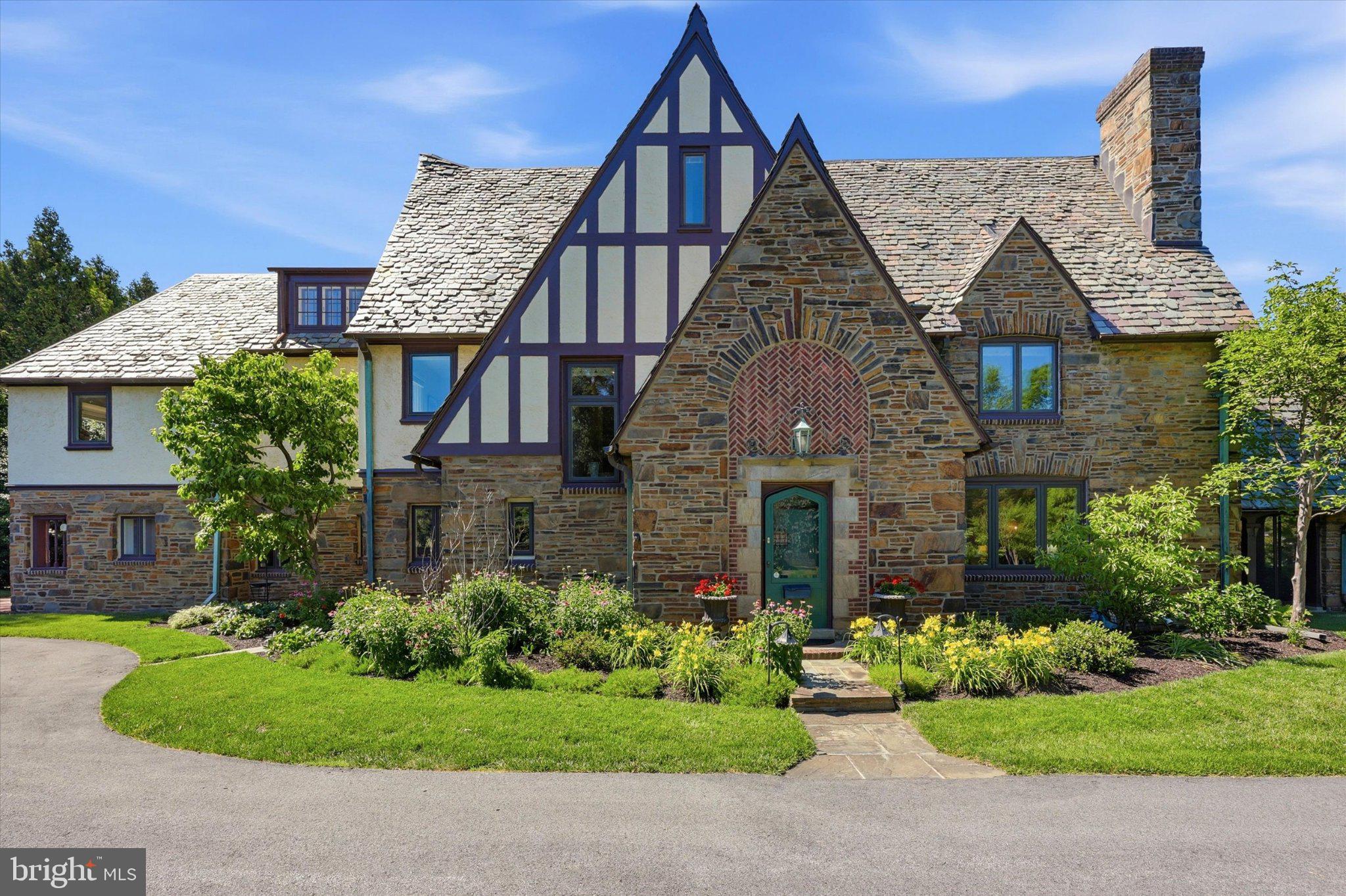 Welcome to 1444 County Line Road, a distinctive stone Tudor that flawlessly combines timeless architecture, classic craftsmanship, and a versatile floor plan designed for both everyday living and entertaining. The dramatic Tudor façade, steeply pitched slate rooflines, half-timbered detailing, intricate arched brickwork, and handsome stone-and-brick entry create an unforgettable first impression. Upon entering the welcoming Foyer, a beautiful staircase, hardwood floors, a generous coat closet, and formal Powder Room set the tone for the home. The sun-filled formal Living Room features windows on three sides, built-ins, and a gas fireplace, creating an inviting space for entertaining and relaxing, with direct access to the screened-in front porch. The formal Dining Room, accented by chair rail and crown molding, flows naturally into the Butler’s Pantry, where ample cabinetry and counter space provide a convenient extension of the Kitchen. The well-appointed Kitchen features a sizeable Pantry, stainless steel appliances, gas cooking, and views of the beautiful rear and side gardens. Just beyond the Kitchen, the Family Room offers a cozy retreat, complete with back stairs to the second floor and access to a private rear patio overlooking the yard. A 1/4 Bath and designated Laundry closet complete the main level. The Second Floor, with hardwood flooring throughout, offers five Bedrooms and three Full Bathrooms. The inviting Primary Suite features ample windows, a walk-in closet, a gas fireplace, and an en-suite Bathroom with a double vanity and glass-enclosed shower. Two additional Bedrooms share a convenient Jack-and-Jill Bathroom with a shower/tub combination, while a rear Bedroom, with access to the back stairs and a full hall Bathroom, offers an ideal Guest Suite. The fifth Bedroom, located off the main hallway, provides flexibility as either a Bedroom or a wonderful home Office/Study. The Third Floor offers endless possibilities, with space that could be utilized for additional Bedrooms, Bathrooms, a Home Office, Playroom, Studio, or additional storage. Outside, the established gardens and grounds are a true highlight, with mature plantings, colorful garden beds, manicured lawn, and inviting outdoor spaces that complement the character of the home. A detached two-car Garage with Loft space provides additional storage and even more potential. 1444 County Line Road is truly a special Main Line property, offering exceptional architectural character, beautiful grounds, generous living space, and a highly desirable location within the Radnor School District. Ideally situated within close proximity to downtown Bryn Mawr, the train station, and the many shops, restaurants, and amenities of the surrounding Main Line, this is a home that must be seen to be fully appreciated.