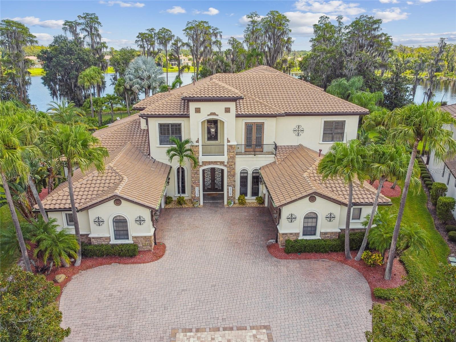 This beautiful lakefront home is truly one of the standout properties in all of North Tampa. Sitting on a private lakefront lot with over 300 feet of shoreline, it offers a peaceful, private setting that feels like your own personal retreat. Behind the gates, the home was custom built with care, combining classic craftsmanship with the kind of amenities you’d expect at a luxury resort. When you walk in, the home immediately welcomes you with its grand two-story foyer. Sunlight pours in through a huge picture window, giving you an instant view of the lake. Rich wood floors, detailed trim, tray ceilings, designer lighting, and a gorgeous wrought-iron staircase all set the tone for a home that is elegant yet inviting. A beautiful stone fireplace adds warmth and charm to the main living area. The kitchen is truly a chef’s dream. It’s designed for people who love to cook or entertain with two Wolf ranges, Sub-Zero refrigeration, Fisher & Paykel dish drawers, custom cabinetry, and a hidden walk-in pantry that even includes a wine fridge. The kitchen opens right into the living space, and brand-new 10-foot impact glass sliders fold open to bring the outside in. Step outside and you’ll feel like you’ve entered your own private resort. The 12-foot-deep, gas-heated pool features a rock waterfall, spa, sun shelf, swim-up table, and even cooling misters for hot days. Tropical landscaping surrounds you, and the lake creates the perfect backdrop. The covered lanai includes an outdoor kitchen, a cozy gas fireplace, and a dedicated pool bath that features both a sauna and a steam shower perfect for relaxing or entertaining friends and family. Upstairs, the large game and media room is designed for fun. It includes a built-in bar, multiple TVs, a new projector and screen, a gas fireplace, and a private balcony overlooking the pool and lake. A spiral staircase connects the balcony to the backyard so the fun can flow indoors or out. The primary suite feels like a peaceful getaway. Oversized bay windows give you sweeping lake views, and a double-sided gas fireplace adds a romantic touch. The spa-style bathroom includes marble finishes, dual vanities, a soaking tub, and an oversized shower with four shower heads. All of the additional bedrooms come with private bathrooms and walk-in closets, making them comfortable for family or guests. The home also includes a spacious office with French doors for anyone working from home. Important improvements have already been taken care of for you, including a 2020 roof, whole-house surround sound, new exterior lighting, two newer pool pumps, plantation shutters, detailed millwork, and a full security camera system that stays with the home. With unmatched craftsmanship, thoughtful features, and a one-of-a-kind lakefront setting, this home offers a luxury lifestyle that’s both elegant and truly comfortable. It’s a place meant to be enjoyed and cherished for many years to come.