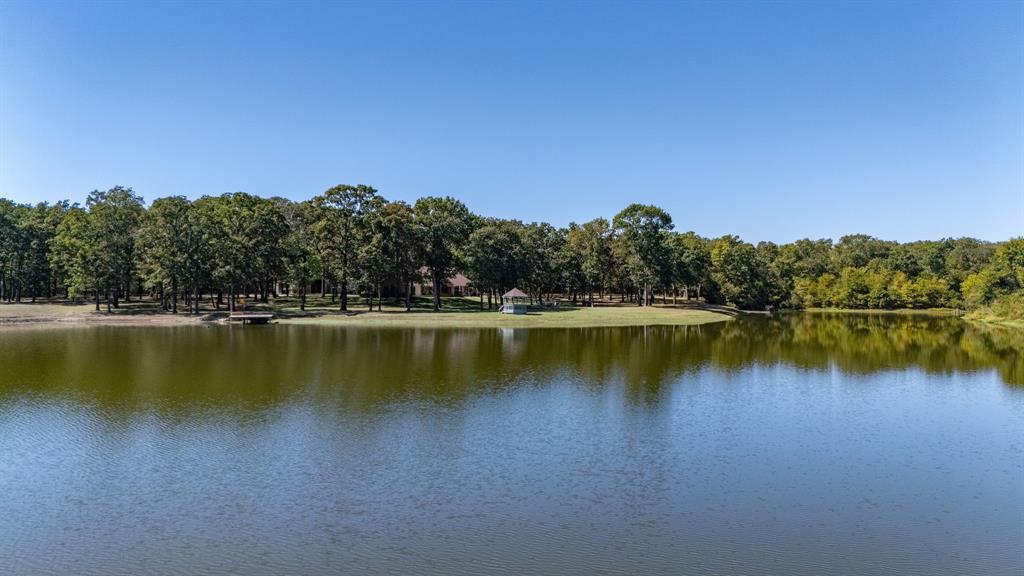 A rare blend of luxury, comfort, and park-like settings on a gated 64-acre estate with a private lake, fully remodeled 4 bedroom, 4 bath main residence, and 600 square feet guest quarters! Escape the traffic and bring your fishing poles or kayak to your own professionally-maintained 7-acre Trophy Bass Lake. From the main residence, you'll enjoy panoramic water views from two porches and an open floor plan, inside. The kitchen includes new quartz countertops, stainless steel appliances, double oven, gas cooktop, and more! A game room and exercise room can be used as additional living areas, office, or flex space. Additional perks are a sauna, 3 central HVAC systems, Reverse-osmosis drinking water (house & barn), misting systems, electric gate with lighted entrance, and ADT security. Inside the 3,000 square feet barn, you'll find 2 remote-operated overhead doors (14x12 each), built-in shelving, entertaining space, and 2 RV hookups (30-amp & 50-am) with sewer. A 600 sq.ft Barn Apartment includes a kitchen with granite countertops, bedroom, living room, full bath, and Central HVAC. Bonus--all have access to FIBER OPTIC Internet! Outside, you'll appreciate the fire pit, new deck & fishing pier with boat dock, 2.5 acres of irrigated yard, Bluegill and Largemouth Bass (up to 9lbs recorded!), meticulously maintained grounds, and transferrable timber AG-exemption. Abundant wildlife provides hours of delight from bird watching (with hundreds of species), to sightings of white-tailed deer, wild turkey and ducks, bald eagles, or owls. Relish the wonders of nature in this pristine oasis, only 72 miles from downtown Dallas. Between the spacious 4,112 main home, manicured 64 acres, and private lake, you'll be the envy of family and friends with this enchanting retreat in Cumby, Texas! Sold fully furnished, move right in and start enjoying the peaceful setting, wildlife and ranch life on day one.