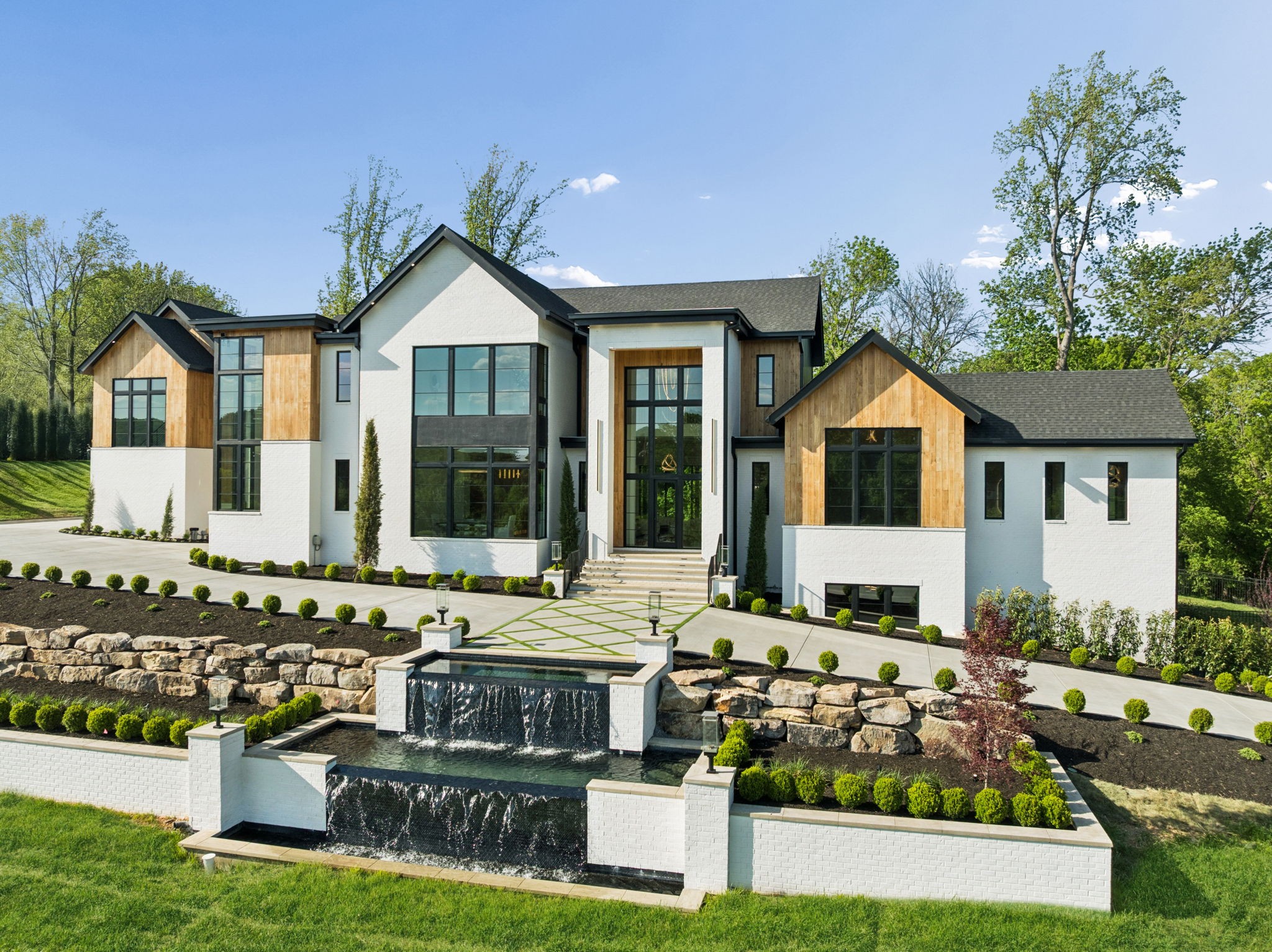 This exceptional new construction estate by 786 Properties redefines luxury living in Bella Collina. Spanning approx. 9,627 sq ft with 7 bedrooms, 8 full baths, and 1 half bath, the home captures sweeping views of Brentwood’s rolling hills. Designed with a warm contemporary aesthetic, the residence features 13.25’ ceilings throughout, 10’ solid white oak interior doors, hand-scraped white oak floors, and custom white oak cabinetry by Carter Interiors/Kemp Cabinets. The kitchen, designed by Helen Hannah, is complemented by a fully equipped chef-caliber scullery and luxury Miele, Beko, and Jenn-Air appliances. Additional highlights include 3 laundry areas, a well-appointed 1-bedroom guest apartment, and a storm shelter room. The main living area is anchored by a striking elliptical Arcus-Stone fireplace with a wraparound floating staircase, while a glass cylindrical elevator adds a dramatic architectural element. A state-of-the-art theater room features an Epson 4K laser projector, Dolby Atmos 7.1 surround sound, 8K screen, and built-in Klipsch speakers. A private gated entry from Concord Rd sets the tone, leading to an architectural waterfall feature at the front entry and extensive, thoughtfully designed landscaping with water elements. The outdoor living is nothing short of resort-caliber, featuring a heated, saltwater infinity knife-edge/zero-entry pool with smart technology and UV sanitation by Liquid Dynamics, an oversized spa seating 12, and a stunning outdoor living area designed for entertaining. Enjoy a fully equipped outdoor kitchen with swim-up pool bar, custom pool decking, travertine patio surfaces, Trex decking balconies, and Techo-Bloc porch surfaces—all enhanced by an integrated outdoor smart system and stunning fire features that create an unforgettable ambiance day or night.