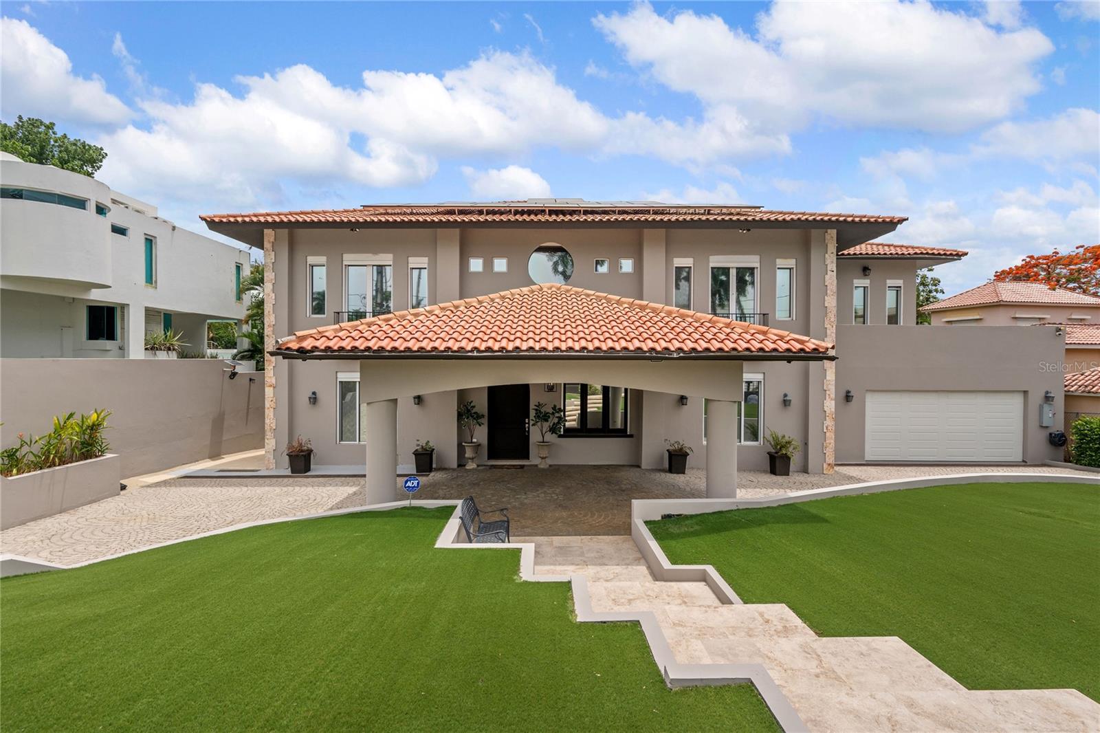 Located on Calle Orquídea in the sought-after Urb. Santa María, this impressive Mediterranean-style residence offers timeless architecture, grand scale, and exceptional living spaces. With 6,417 SF of living space and 13,048 SF of total construction, the home features soaring ceilings over 30 feet high, marble floors, elegant architectural details, and expansive interiors designed for both everyday living and entertaining. The residence offers four spacious bedrooms, including a remarkable primary suite with a private balcony and oversized bathroom featuring a jacuzzi and separate shower. A tavern-style basement with a rustic wine cellar creates a unique entertainment space, while a separate bonus structure with its own bathroom offers added flexibility. Complete with an elevator, gazebo, solar panel system, and four backup batteries. This is a truly distinctive property within an amenity-rich community featuring tennis and basketball courts, a soccer field, and multiple playgrounds. Ideally located near top private schools, restaurants, supermarkets, and everyday conveniences, the home offers an exceptional lifestyle in one of San Juan’s most sought-after communities.