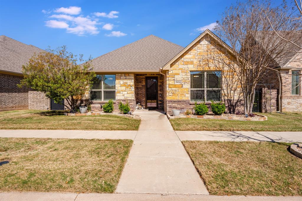 Welcome to effortless living in the gated, sidewalk-lined community of Fountain Village—where comfort, convenience, and low-maintenance living come together beautifully. This thoughtfully designed single-story brick and stone home offers 3 bedrooms, 2 bathrooms, and a 2-car garage, all surrounded by beautifully landscaped grounds. Step inside to an open-concept layout filled with natural light, soaring vaulted ceilings, and large windows that create a bright, airy feel. Wood-look tile flooring throughout the main living areas adds both style and durability. The spacious living room is anchored by a stunning floor-to-ceiling stone fireplace, complemented by a wood-beamed vaulted ceiling and matching mantle that adds warmth and character. The kitchen is designed for both everyday ease and entertaining, featuring abundant granite countertops, white cabinetry, double ovens, a gas cooktop, built-in microwave, breakfast bar seating, and a generous walk-in pantry. It flows seamlessly into the dining and living areas, making gatherings feel natural and comfortable. The private primary suite is a relaxing retreat with direct access to the patio—perfect for morning coffee or quiet evenings. The ensuite bath offers dual vanities and a large walk-in shower with dual sprays for a spa-like experience. Two additional bedrooms provide flexibility for guests, hobbies, or a home office. Enjoy outdoor living under the stunning vaulted ceiling of the large porch inside the fully fenced, low-maintenance yard designed for privacy and relaxation. A spacious laundry room with sink adds everyday convenience. Foam insulation enhances energy efficiency and year-round comfort. The HOA enhances the easy living lifestyle by maintaining the front yard, gated entry, and trash service, while also offering a community pool and clubhouse for socializing and recreation. Move-in ready and designed for easy living—this home lets you spend less time maintaining and more time enjoying life.