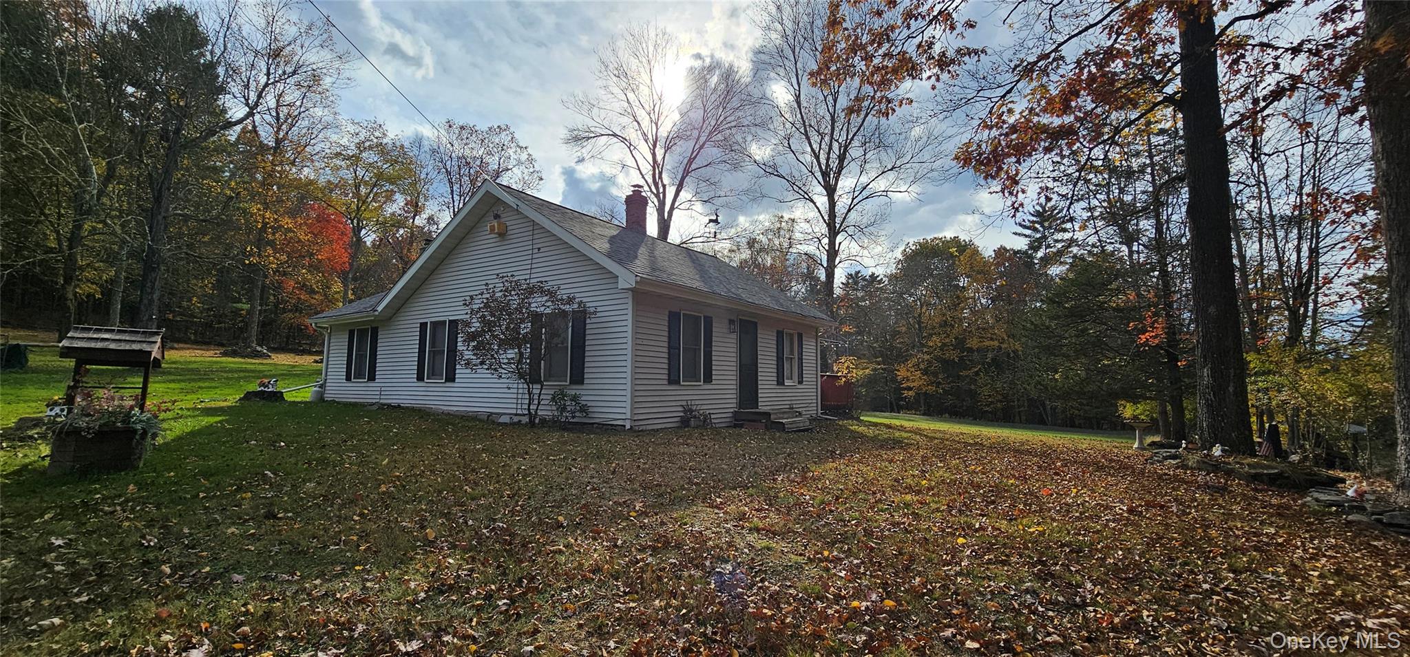 View of property exterior with a lawn, a shingled roof, a chimney, and a forest view