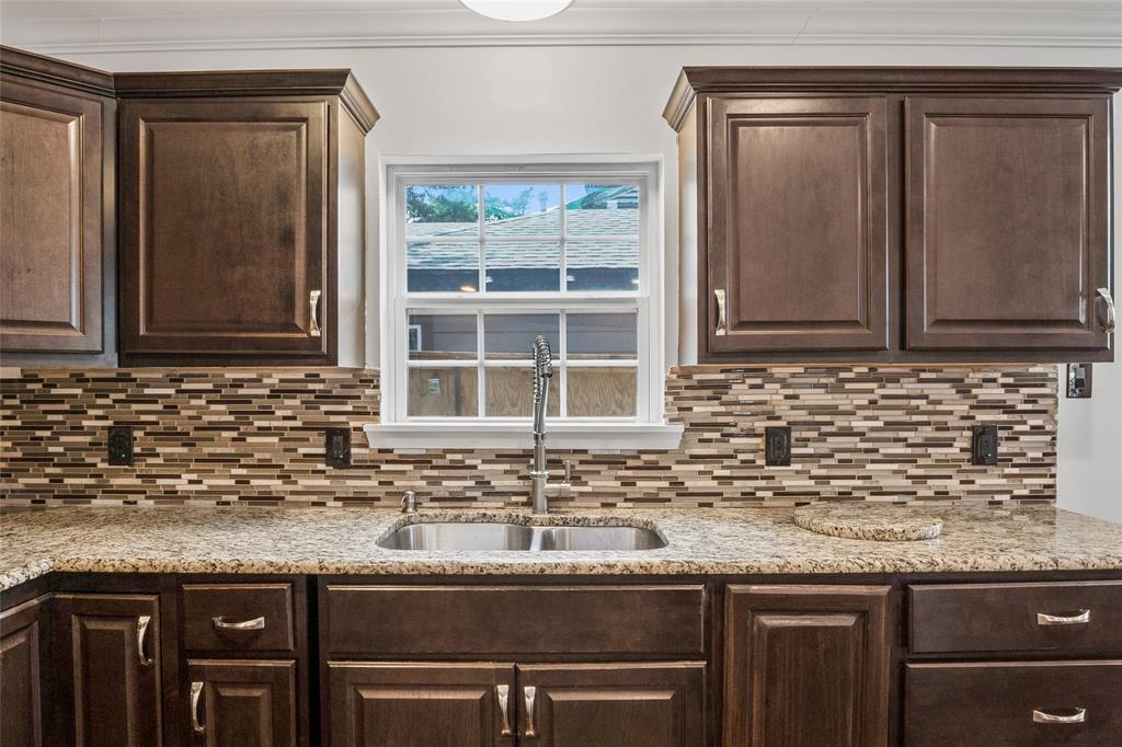 Kitchen with dark brown cabinetry, light stone counters, andbacksplash