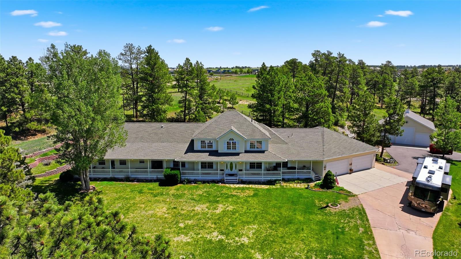 2 Separate Homes!! Welcome to 7550 N Village Road – This exceptional MULTI-GENERATIONAL ESTATE is designed for modern flexible living and includes a main residence plus a 1318 sq. foot attached 1-bed/1-bath + office ADU, connected by a breezeway and front covered porch — perfect for extended family or long-term guests while keeping everyone comfortable and independent. Together these spaces deliver approximately 6,760 total sq ft with 27 rooms, including 6 bedrooms and 5 full baths. From the dramatic two-story entry, you enter the main home. On the main level you’ll find the primary suite plus a secondary bedroom whose ensuite bath opens both to the bedroom and hallway. Also on this level are a dedicated office and formal dining room. The open-concept kitchen anchors the home and flows into the two-story family/great room with a gas fireplace and double doors to the backyard. Just off the kitchen dinette is the laundry room with plentiful cabinetry and a large soaking sink. Upstairs are two additional bedrooms, a full bath and a large loft with incredible Pikes Peak views! The finished basement includes an additional bedroom and full bath, game room, family room, built-in dance floor/open rec. space and large storage room. Accessible from the main home is a massive attached 4-car garage with an additional 15 × 25 workshop — ideal for vehicles, hobbies or business. Outside the lifestyle continues: the land is zoned for horses, with rolling meadows, mature ponderosa pines and abundant wildlife. A DETACHED 50 × 50 1974 sq. foot GARAGE/BARN with cement floor, three 10-ft and one 14-ft overhead doors, tack room and loft adds serious utility. The grounds feature an incredible WATER FEATURE, fire-pit, covered outdoor kitchen with gas grill, porch and deck — and from the front covered patio you’ll enjoy PANORAMIC VIEWS of Pikes Peak and Colorado skies. A recently asphalted public road into this coveted private neighborhood enhances infrastructure and curb appeal.