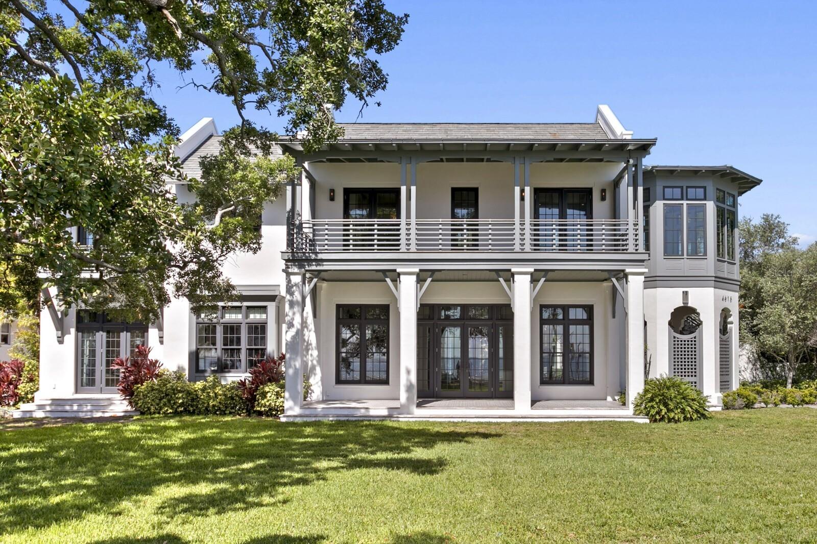 Positioned along scenic Bayshore Boulevard on a rarely found .6-acre lot, this 2018-built British West Indies-inspired water view residence offers an exceptional combination of newer construction, generous grounds, and timeless architectural design in the heart of South Tampa. Designed by Cooper Johnson Smith, the home showcases refined craftsmanship throughout, from the distinguished slate roof to the Venetian plaster walls, creating a residence that feels both elegant and inviting.  A gracious floor plan unfolds beneath soaring 12-foot ceilings, where transom windows and walls of glass French doors bring in natural light and frame views of Tampa Bay and the private courtyard pool from nearly every room. Designed for both everyday living and memorable entertaining, the main level features open kitchen, dining, and living areas, while a large media/great room offers an impressive entertaining bar, walk-in wine room, and seamless same-level access to the outdoor patio and pool areas. The gourmet kitchen is a true culinary centerpiece, appointed with a striking ILVE Italian range, Sub-Zero refrigeration, dual dishwashers, and custom inset cabinetry. A private office with custom built-ins overlooks the bay, while two powder baths and a spacious utility and laundry room add function and ease to the main level. Upstairs, the primary suite offers a serene retreat with panoramic sunrise views over the bay. An octagonal sitting room with a private beverage bar creates an ideal space for morning coffee, a secondary office, or a quiet place to unwind. The spa-inspired primary bath features dual vanities, a freestanding soaking tub, a seamless-entry shower, and a private water closet. Both the bedroom and bath open to a covered front veranda, while the expansive dressing room includes floor-to-ceiling custom cabinetry, a center island, and direct access to an additional upstairs laundry. Three additional ensuite bedrooms provide comfortable accommodations, each with private baths and picturesque views of either the open water or the courtyard pool. Connected by a covered upper-level walkway, the detached in-law/guest retreat includes a fifth bedroom, living room, and full bath, offering an ideal setup for extended guests, multigenerational living, or a separate lounge space. Outdoors, the property delivers a true private resort experience, enhanced by the scale of its more than half-acre homesite. The covered lanai wraps around the pool and spa, complemented by an outdoor shower, lush tropical landscaping, and a fully appointed outdoor kitchen with gas grill and island dining. The expansive grounds create a level of privacy, space, and livability that is especially rare along Bayshore Boulevard. Additional features include a 5-car garage configuration, with a 3-car garage plus a separate 2-car garage, dramatic coffered ceilings, exposed architectural beams, a wet bar, and integrated audio, video, and camera systems. With newer 2018 construction, a substantial lot size, exceptional architectural design, and a premier Bayshore Boulevard setting, this residence stands apart as one of South Tampa’s most distinctive waterfront offerings. The location places you moments from acclaimed dining, shopping, top-rated schools, arts and cultural destinations, sports venues, downtown Tampa, and Tampa International Airport.
