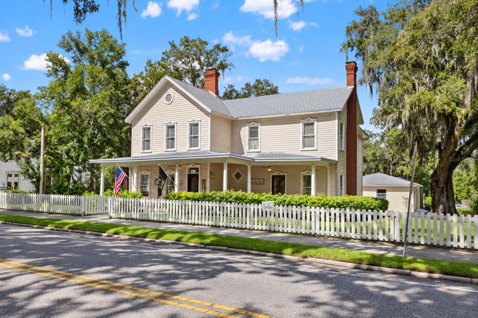 A distinguished piece of Brooksville history, beautifully preserved and extensively modernized. Dating to the 1890s and recognized as the birthplace of Alfred McKethan, one of Brooksville's most notable historical figures, this exceptional downtown residence offers the architectural character of a bygone era with the comfort, functionality, and amenities of a thoughtfully updated home. Situated on an oversized parcel beneath magnificent grandfather oaks, the property is just a short walk from the restaurants, shops, coffee houses, and community events that continue to define the revitalization of historic downtown Brooksville.The impressive two-story residence offers four spacious bedrooms, three full bathrooms, one half bathroom, an executive office, formal dining room, traditional parlor, multiple living areas, and an abundance of covered porch space. Generous room proportions, 10-foot ceilings, substantial windows, and beautifully restored heart pine and hardwood flooring create bright, inviting interiors while maintaining the home's original architectural integrity. Historic details include intricate moldings, shiplap walls, antique fixtures, clawfoot tubs, and five fireplaces, including three gas fireplaces downstairs and two wood-burning fireplaces upstairs.Over the past several years, the owners have completed an extensive series of improvements, bringing the home's restoration to its final stages. The beautifully remodeled kitchen features white cabinetry, elegant countertops, custom tile backsplash, stainless steel appliances, a statement range hood, and generous storage. Additional improvements include remodeled bathrooms, restored wood flooring, fresh interior paint, and carefully selected finishes that complement rather than compete with the home's historic character. Previously updated electrical and plumbing systems, three HVAC units, and a metal roof installed in 2008 add to the property's established improvements.Outdoor living has been significantly expanded with the addition of a beautiful screened-in swimming pool, spacious rear entertaining deck, covered seating areas, and dedicated outdoor recreation space. The elevated rear deck offers convenient access from the home and overlooks the pool and surrounding grounds. A classic white picket fence frames the front lawn, while mature landscaping and sprawling oak trees provide a picturesque setting. The oversized property also includes a detached 24-by-24-foot garage, separate 20-by-14-foot workshop/storage building, additional parking, and a circular driveway.The expansive covered front porch, with its traditional columns and generous seating areas, is a defining feature of the home and an enduring example of Southern residential architecture. It provides a front-row connection to the charm of this established historic neighborhood.The location offers something increasingly desirable: the ability to enjoy a spacious residential property while remaining connected to a growing, walkable downtown. Historic Brooksville continues to attract locally owned businesses, restaurants, boutiques, coffee shops, markets, live music, and community festivals, supported by an active Main Street organization and a strong appreciation for the city's architectural heritage.