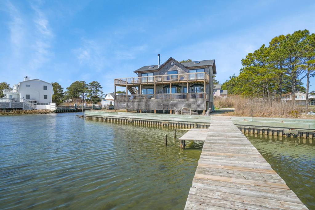 Welcome to this stunning coastal retreat on Chincoteague Island, surrounded by water on 2 sides. This 3-bed + 2 addit'l rooms, 3-bath home offers elegant open-concept living w/ a stone fireplace, cathedral ceilings, a cozy sitting area. Both spaces open to a covered deck w/ breathtaking bay & Assateague Island views—perfect for entertaining. The modern kitchen features a breakfast bar & SS appliances. The main level includes a bedroom & full bath, while upstairs, the primary suite has a private bath. Two bay-facing rooms open to a second-story deck w/ stunning water views. Outside, enjoy crabbing, fishing, or kayaking from the dock. A shed adds functionality, & an adjacent wooded lot offers expansion potential. Experience the ultimate coastal lifestyle in this waterfront sanctuary. NO HOA!
