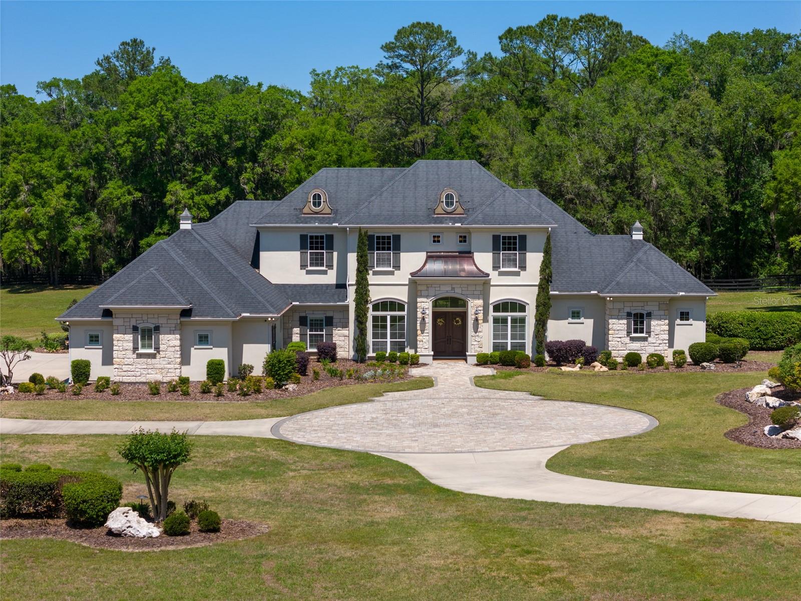 Welcome to this stunning luxury home in the exclusive, gated community of Wyndsong. Built by Tommy Waters and sitting on 5 beautifully landscaped acres, this custom residence features high ceilings, extensive built-ins, and an open-concept layout that seamlessly blends everyday living with high-end entertaining.The kitchen offers two walk-in pantries, premium appliances, and a large island that overlooks the living area, complete with custom finishes and in-ceiling speakers for music or surround sound. Just beyond the living space, the game room is an entertainer’s dream, featuring a wine storage and wet bar. A dedicated home office with built-in cabinetry and desk provides a stylish and organized workspace.Upstairs, you’ll find a spacious loft that connects two bedrooms with a Jack and Jill bathroom, plus a climate-controlled flex/storage room that can easily be transformed into a studio, office, bedroom, or more.Step outside to a saltwater pool and hot tub, paired with a summer kitchen and bar, perfect for hosting. Toward the back of the property, a fire pit creates a cozy space for gatherings on cooler nights.Additional upgrades include an oversized 4-car garage, two zoned HVAC systems, and a whole-home Generac generator for peace of mind during hurricane season. The home is also has excellent insulation in 2 attic spaces and to keep the house cool in the summer, along with 4 gas fireplaces placed throughout the house for the chilly winter days.The Wyndsong community offers peaceful walking and horseback riding trails, adding to the lifestyle appeal.This rare property combines privacy, space, and luxury. Come see for yourself!