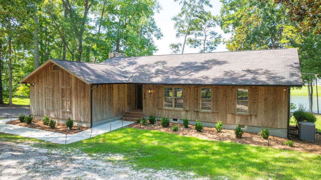 Waterfront home in established neighborhood close to everything with no HOA fees! This striking 3 bed/ 2.5 bath lakeside cabin offers all the luxuries of living in the countryside while still remaining close to town. It's only 4 minutes away from Publix, Lowes, and other shopping! The house comes with a spacious back deck that is the perfect place for grilling dinner with friends and family. Walk down to the dock and enjoy easy access to fishing and swimming in the lake. Cuddle up by the fireplace with your loved ones in the cozy and spacious living room while enjoying the stunning lake view and the sunset from the floor to ceiling windows. The chef's kitchen is perfect for cooking for guests and includes a stainless steel refrigerator, oven, cook top, wine cooler, a large island, and lots of pantry space. Game nights and dinner parties will be incredible in the beautiful formal dining room. The primary suite is very spacious and include lots of closet space and a new tiled walk in shower.  Downstairs, the spacious den with fireplace and half bath offers comfort, extra space,  and storage with a large heated and cooled workshop. The downstairs den could easily be a 4th bedroom. The details are what make a house feel special, and with cypress exterior siding, vaulted ceilings, warm cypress wood paneling, and sliding glass doors, this home is full of character and charm.
