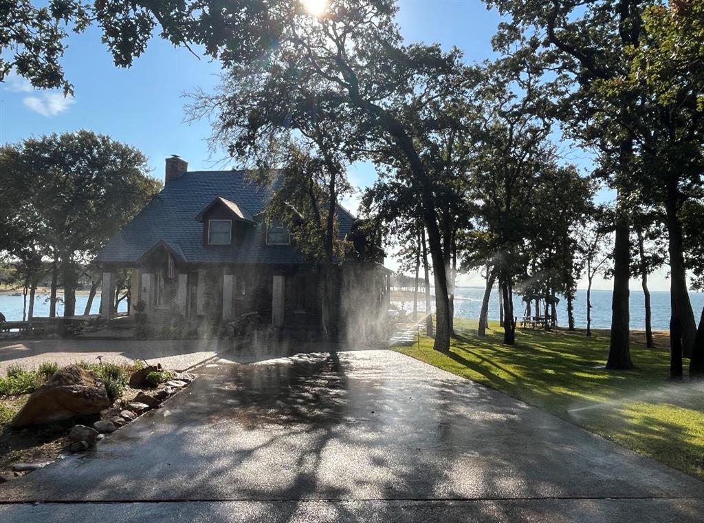 A charming tree-shaded retreat where morning sunlight filters trough the oaks and dances across the water. This inviting home sits just steps from the shoreline, offering panoramic lake views from almost every angle. A gently curving driveway from the private gated entry leads you through beautifully maintained landscaping and welcomes you to a warm, craftsman-style residence with classic dormer windows and a spacious front porch.Inside, natural light pours in, creating a calm and airy atmosphere perfect for relaxing weekends. Outside, the expansive lawn stretches toward the water, providing ample space for gatherings, lakeside lounging, or quiet evenings watching the sunset. With mature trees, a peaceful setting, and direct lake access, this property offers the ideal blend of privacy, beauty, and lakeside lifestyle. Whether you envision it as a family getaway, retirement sanctuary, or year-round home, this lakefront haven delivers the perfect backdrop for unforgettable memories.