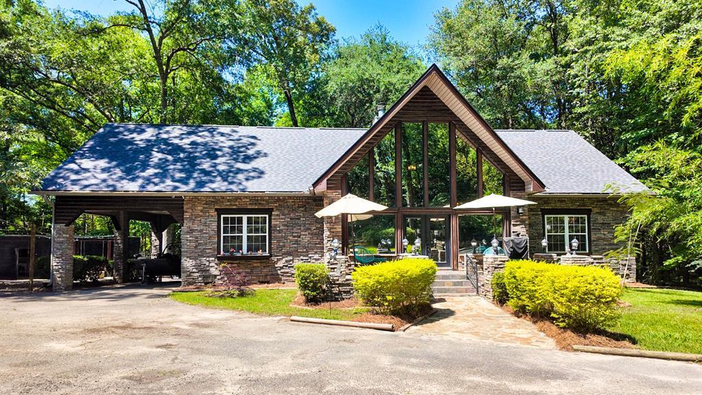 This stunning 4-bedroom, 4 bath stone and log home sits on nearly 4 private acres overlooking a shared 6-acre lake, combining rustic elegance with modern upgrades. A circular driveway leads to a spacious 4-car garage and an inviting entrance, where you'll find floor-to-ceiling stonework and a double-sided fireplace with a cypress stone mantle. The great room and dining area feature a wall of windows and soaring 20-foot tongue-and-groove cypress ceilings, flooding the space with natural light and scenic views. The main-level master suite includes a private office overlooking the lake and a luxurious ensuite bath. Each bedroom offers its own full bathroom, including the upstairs rooms which feature pine ceilings, pine floors milled from the property, and large dormers ideal for office or play areas. The oversized kitchen is a chef's dream, with custom hickory cabinetry, a walk-in pantry, floating island, picture windows, and new appliances. The screened back porch is the place to unwind and take in the views. The property also has a screened addition with a bar for hanging out with friends or family and an additional screened area perfect for a hot as well as a screened lakeside area to enjoy the scenery. A versatile loft upstairs makes a great game or lounge area. The detached ~1,800 sq ft 4-bay garage includes a floored storage attic, blown-in insulation and could be future living space. high ceilings and utility sink. Recent updates include a brand-new roof on both home and garage, new sod, sheetrock and paint upstairs, a firepit with swings, water drainage system, water softener on the well, , and night/day window tint that enhances views while ensuring privacy. With a vapor barrier and dehumidifier under the home you can ensure this home is protected. This exceptional property blends craftsmanship, comfort, and lakeside tranquility—offering a one-of-a-kind retreat with room to grow.