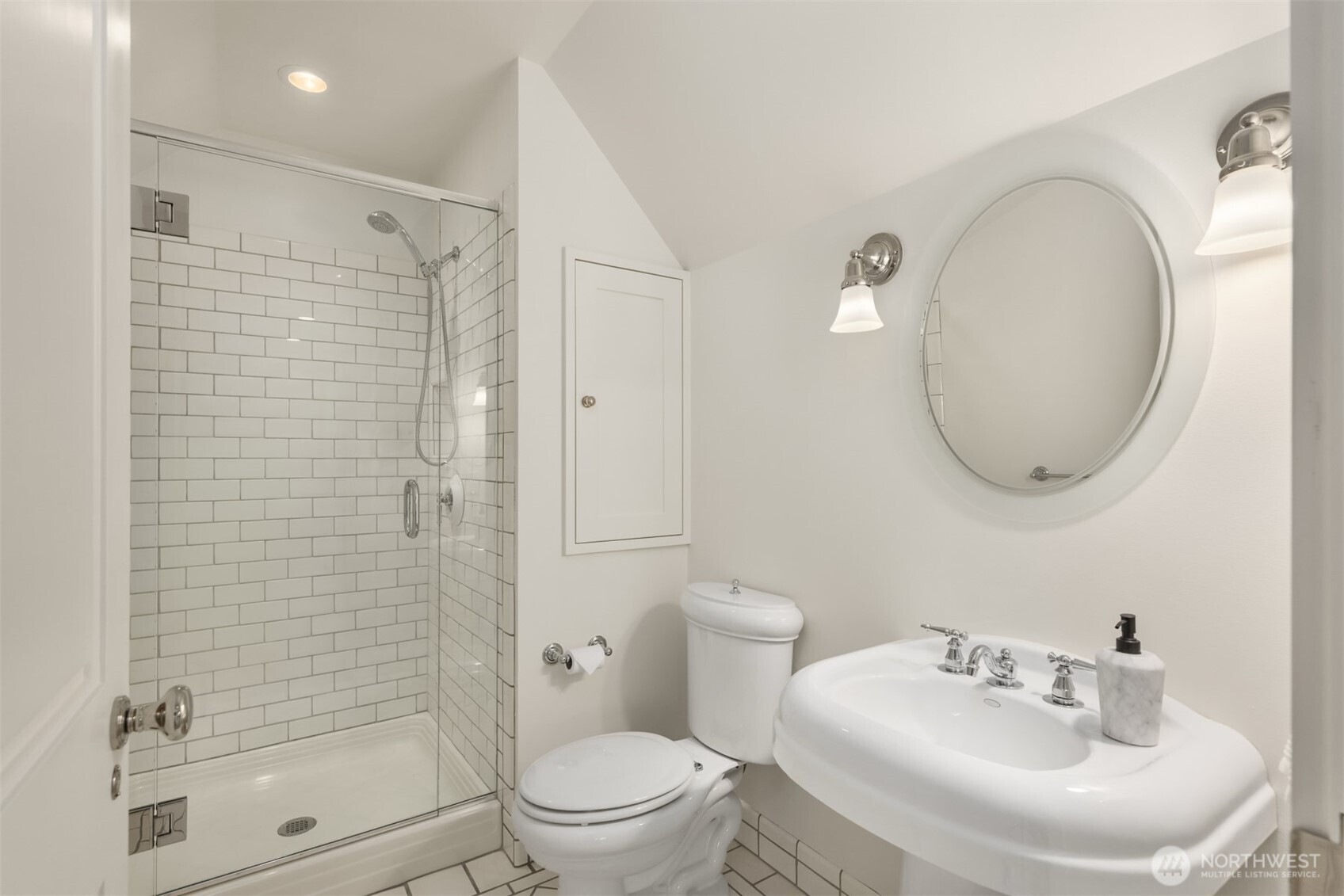 Bright bath featuring a glass-enclosed shower and a round mirror.