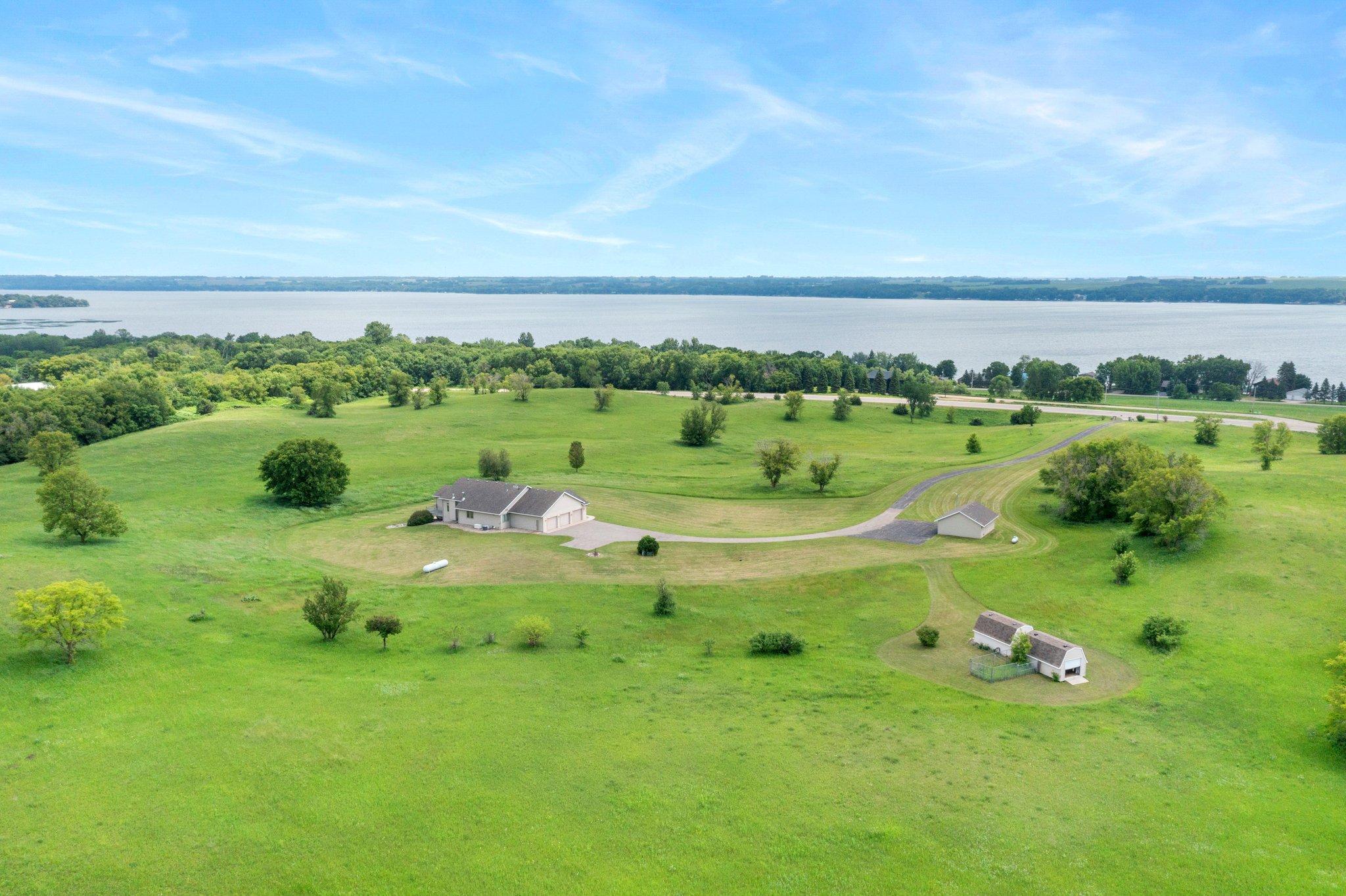 Discover one of Starbuck’s best-kept secrets—an extraordinary 3-bedroom, 3-bathroom residence set on over 34 acres of rolling hills, woods, and meadows. This private retreat offers an unmatched combination of natural beauty, tranquility, and space, making it ideal for those seeking a peaceful lifestyle deeply connected to nature. A private, quarter-mile asphalt driveway welcomes you into the heart of the property, revealing panoramic views of Lake Minnewaska. The lake’s crystal-clear blue waters stretch across the southern horizon and are visible from multiple points throughout the home and land—especially from the hilltops. Though secluded, the property is just a 3-minute drive to the Starbuck marina, offering quick access to boating, fishing, and lakeside recreation. The home is designed for comfortable, luxurious living. The kitchen is a chef’s dream, with abundant custom cabinetry, expansive Corian countertops, a peninsula with breakfast bar seating, and brand-new stainless steel appliances. Italian tile flooring and vaulted ceilings add elegance, while a bay window in the informal dining area fills the space with natural light and picturesque views. A formal dining room offers Italian marble flooring, a classic chandelier, and two large windows, making it perfect for special gatherings. The main-level living room boasts high ceilings, a gas fireplace with rich wood and Italian marble surround, and sliding doors that lead to a 14x9 deck—perfect for indoor-outdoor entertaining. The primary bedroom features premium Italian tile flooring and a private en-suite bath with an Italian-designed jacuzzi tub, single vanity, linen closet, and spacious 8x8 walk-in closet. Two additional main-level bedrooms also offer premium tile floors, generous closet space, and are conveniently located near a full bathroom. A main-level laundry room with built-in cabinetry connects to a finished, heated three-car garage with attic access. For even more versatility, a second detached two-stall garage is fully finished, insulated, and heated, with two separate storage rooms ideal for hobbies or seasonal storage. The expansive lower level is designed for entertaining, with an open-concept layout including a family room, recreation area, and a custom bar with a glass block backdrop and built-in shelving. Walkout access leads to a large concrete patio—perfect for gatherings. Additional features on the lower level include a spacious office with dual closets, a ¾ bathroom with walk-in shower, two flex rooms suitable for a gym or hobbies, a 20x5 storage room, and a 16x12 panic room for added security and utility. Modern amenities enhance both comfort and peace of mind: Signature Pella triple-pane windows, artisan hand-textured ceilings, a Beam central vacuum system, two zoned furnaces, and a whole-house backup generator with automatic activation. High-speed fiber optic internet ensures seamless connectivity, and a state-of-the-art Heartland Security system with smart features provides comprehensive protection. Two large outdoor storage sheds offer additional space for tools and equipment. Whether you're exploring the land, enjoying the views, or relaxing indoors, this property offers a rare blend of privacy, natural beauty, and high-end features—an exceptional opportunity in one of Starbuck’s most desirable locations.