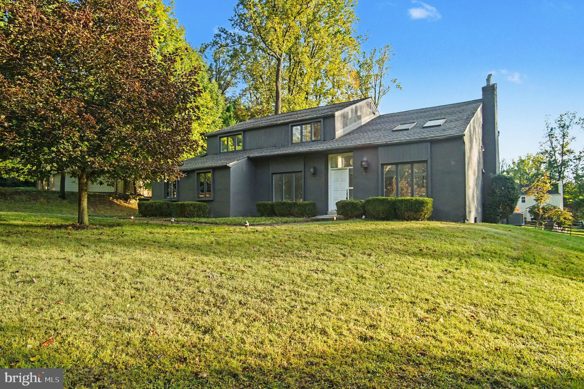 3 Harvey Ln is a two-story Newtown Square home with four bedrooms, three full bathrooms, one half bathroom and 3,085 square feet of living area. White cabinetry with blue trim surrounds the kitchen island, double wall ovens and sink beneath a window. Tall ceilings, skylights and an open upper gallery distinguish the main living spaces, with a separate dining room and curved-window sunroom nearby. The primary suite includes a fireplace sitting area and a bathroom with dual sinks and a tub. A rear deck overlooks wooded grounds, and an attached two-car garage provides enclosed parking. An unfinished basement adds separate space below the living area.