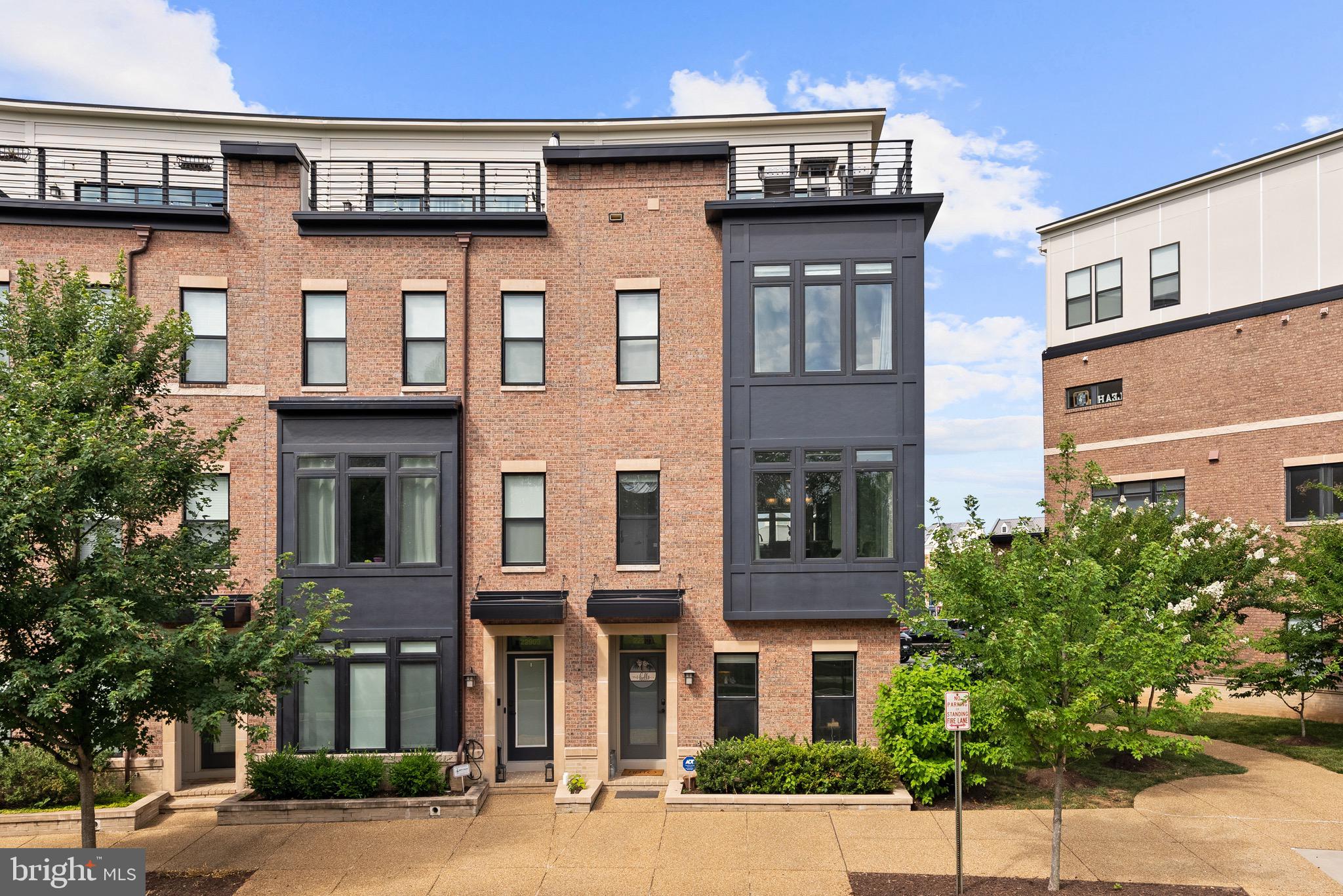Perfectly positioned in one of Brambleton's most coveted locations, this exceptional luxury end-unit townhome offers the rare combination of walkable convenience and peaceful surroundings. Just steps from Brambleton Town Center's shopping, dining, entertainment, and year-round farmers market, yet directly across from a beautiful park, you'll enjoy vibrant urban living with tranquil green views and a level of privacy seldom found this close to everything. Situated on a premium corner homesite, this rarely available larger end unit is bathed in natural light through expansive walls of windows, creating bright, airy living spaces throughout. Offering 4 bedrooms, 3 full baths, 2 half baths, a two-car garage, and an incredible rooftop terrace, this home seamlessly blends luxury, comfort, and an unbeatable location.Designed with exceptional craftsmanship and nearly $100,000 in premium upgrades, the home showcases 5-inch engineered textured hardwood flooring, custom window coverings, French doors leading to a private office, a wood-plank fireplace feature wall, and custom built-in bookcases and cabinetry that anchor the family room with warmth and style.The spectacular chef's kitchen is a true showpiece, featuring professional-grade Wolf appliances, including a 6-burner gas range, wall oven, and microwave, along with a Sub-Zero refrigerator, Asko dishwasher, an expansive waterfall granite island, and an additional wall of custom pantry cabinetry that delivers exceptional storage and functionality.The luxurious primary suite and baths continue the home's elevated design with quartz countertops in the primary bath, granite countertops in the guest baths, and designer tile flooring and shower surrounds throughout.The versatile upper-level loft offers the perfect fourth bedroom, guest suite, media room, or flex space, highlighted by an exposed brick accent wall and a stylish sliding barn door.Designed for exceptional entertaining, the rooftop terrace—your own private "yard in the sky"—features a built-in fireplace, integrated outdoor speakers, and generous space to dine, relax, and gather with friends. Dual-zone built-in wireless ceiling speakers provide seamless audio throughout the home, while the finished two-car garage offers luxury vinyl flooring, metal storage cabinetry, and overhead storage racks for exceptional organization and functionality.Combining one of Brambleton's premier locations with a rarely available larger end-unit design, expansive walls of windows, nearly $100,000 in upgrades, and luxury finishes throughout, this is a rare opportunity to own one of the neighborhood's most exceptional residences.
