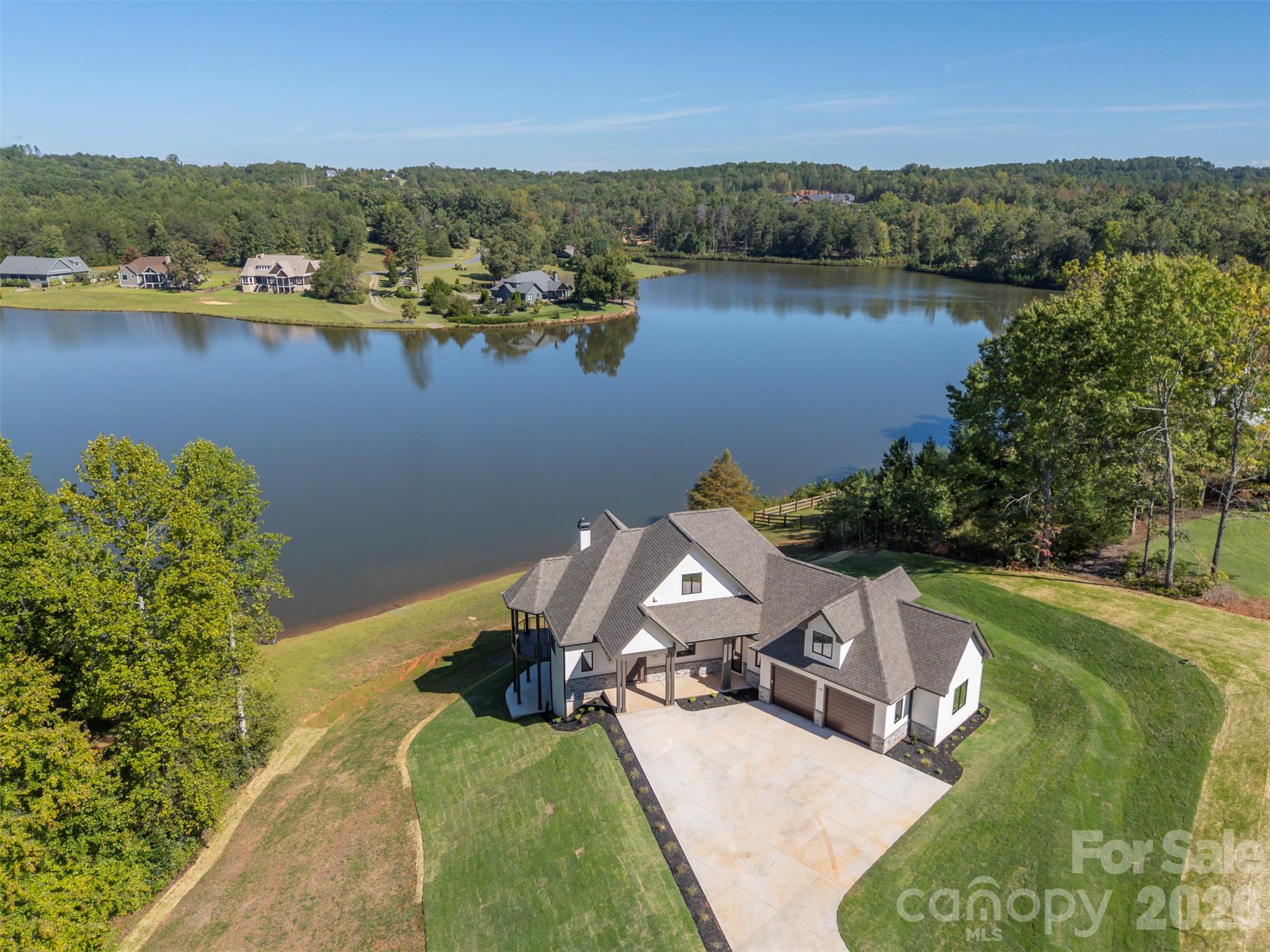 Wake up seeing the water, slip your kayak in before breakfast, and end the day on the balcony as the sun settles over the lake. This brand-new 2026 home offers 159 feet of direct frontage on 33-acre Lake Sandy Plains and sits on 0.89 acres in Derbyshire, a gated equestrian community where the lifestyle is every bit as special as the home itself.Reserved for peaceful, non-motorized recreation, the lake invites you to kayak, paddleboard, swim, or fish just steps from your back door. Beyond the shoreline, Derbyshire offers exceptional equestrian amenities with access to the CETA and FETA trail systems for miles of riding through the beautiful Carolina foothills. Approximately eight miles of community walking trails provide the perfect setting for morning walks with the dog, while the gently rolling lawn leading to the lake offers plenty of room for both two- and four-legged family members to enjoy.Inside, European windows and doors capture the lake views and fill the home with natural light. The main living area soars beneath a vaulted tongue-and-groove wood ceiling, anchored by a handsome stacked-stone fireplace. Glass doors open onto the covered wraparound balcony, where cable railings preserve the sweeping views and create an inviting outdoor living space overlooking the water.The kitchen combines clean, timeless design with thoughtful functionality, featuring white shaker cabinetry, a stained wood island, stone countertops, a Bosch wall oven and microwave, a Bosch dishwasher and a natural gas cooktop, plus a generous walk-in pantry.The main-level primary suite is a peaceful retreat with beautiful lake views, a custom walk-in closet, and a spa-inspired bath with a frameless glass shower. Just off the oversized two-car garage, a practical mudroom is ready for muddy boots and paws, with the laundry room conveniently located alongside.Downstairs, the walkout lower level opens directly to a covered lakeside patio. Designed for relaxed entertaining, it features a spacious recreation room with a modern electric fireplace, wet bar, and wine cellar, plus two additional bedrooms with walk-in closets and a full bath.At approximately 2,942 finished square feet, this home is designed around how you want to live—quiet mornings on the lake, afternoons on the trails, dogs playing in the yard, and evenings watching the light change across the water.All of this is just minutes from Columbus, Tryon, and Landrum, with convenient access to I-26—offering a peaceful lakefront and equestrian lifestyle without giving up easy access to town.