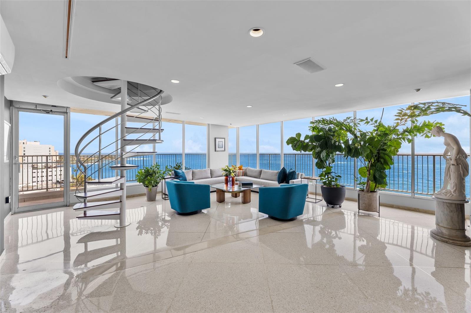 Perched atop Mirador del Condado, where Ashford Avenue meets the open Atlantic, West Penthouse B commands sweeping views of the ocean, Condado Lagoon, and city skyline a residence where every space frames a view.The penthouse offers 3,720 square feet of interior living space with three bedrooms, two full and one half bathrooms, and a dedicated steam room, complemented by an extraordinary 3,870 square foot exclusive use rooftop terrace.The main level unfolds as one continuous, open social space, enclosed by walls of floor to ceiling glass and finished with polished terrazzo floors that extend throughout the living areas. At its center, a sculptural spiral staircase, custom designed and built by Boston Design Group, rises through the living area to the rooftop terrace. Together, the interior and exclusive rooftop terrace offer exceptional space for entertaining and everyday living.The L shaped kitchen with peninsula features quartz countertops, Bosch cooking appliances, a Frigidaire Professional refrigerator, built in wine storage, and a breakfast nook overlooking the Atlantic.The bedroom wing offers privacy and flexibility. The primary suite, created by combining two of the residence’s original bedrooms, includes a sitting and media lounge, lagoon views, and a connecting private office. A second bedroom overlooks the lagoon and skyline, while the third is privately positioned away from the primary wing, with ocean views and flexibility as a guest room or study.Above it all, the exclusive use rooftop terrace offers multiple areas for lounging and entertaining, an outdoor kitchen and bar, and panoramic views across the Atlantic, Condado Lagoon, and city skyline. One level below, a wraparound balcony offers another perspective over the water and skyline.Smart home features include Alexa compatible lighting and Somfy motorized shades throughout, along with hurricane shutters and a whole house water filtration system.Mirador del Condado is a 13 story oceanfront condominium directly on Ashford Avenue, offering 24 hour security and a swimming pool. Condado’s leading hotels, restaurants, and nightlife are within walking distance, with Old San Juan just minutes away.Offered fully furnished and turnkey, Penthouse B includes two enclosed garage parking spaces plus one assigned open parking space. A singular oceanfront residence offering exceptional scale, privacy, and one of Condado’s most compelling vantage points.