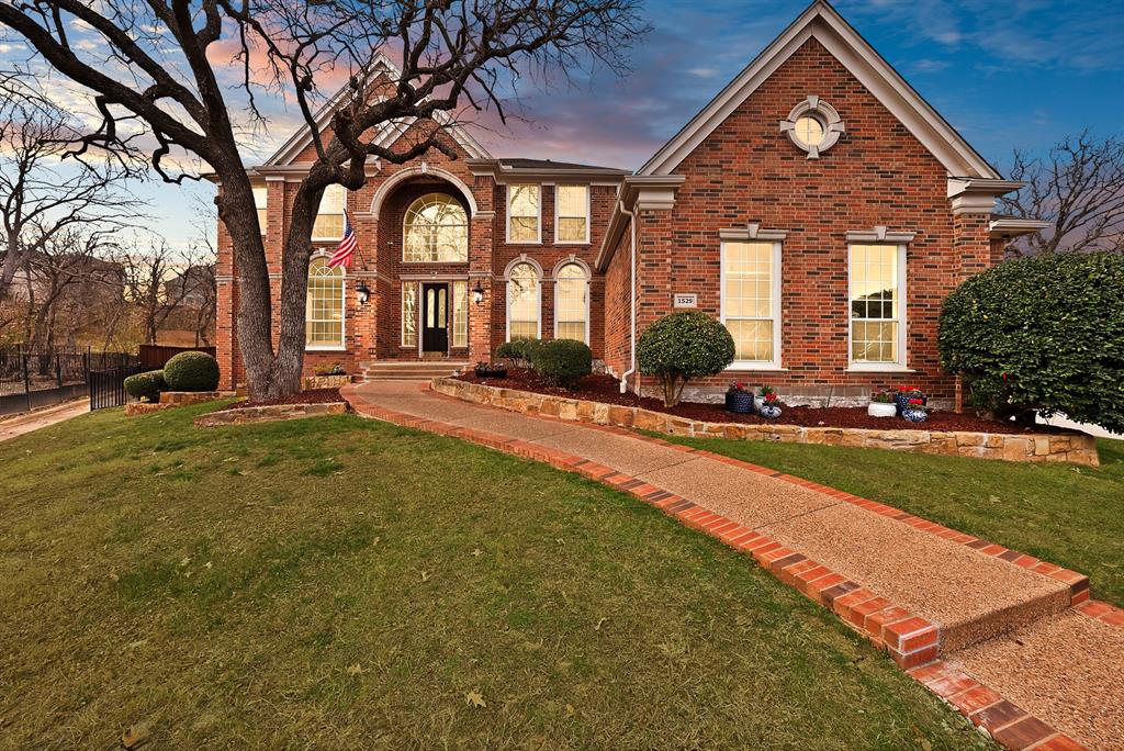Tucked in a quiet cul-de-sac in the established Hudnall Farm neighborhood, 1529 Lost Trail offers the kind of space, privacy, and presence that discerning Keller buyers look for. Set on an elevated .4-acre lot with stone retaining walls and mature trees, the home makes a strong first impression with stately brick elevation, a grand entry, and a large lot creating separation from your neighbors. Inside, over 4,100 square feet unfolds in a thoughtful, traditional layout. The dramatic entry and soaring ceilings define the energy of the home as soon as you walk in. With a winding staircase, a formal dining area and massive windows, the front of the home shines. The kitchen opens seamlessly to the main living area and breakfast nook, offering generous counter space and island seating. The back stairs offer quick access to the second level right from the garage or side entrance. The primary suite is privately positioned on the main level, featuring a spacious bedroom, oversized bath, and an exceptional walk-in closet designed to function as a true dressing room, not an afterthought. A second bedroom and bathroom suite on the first level makes this an ideal mother-in-law floorplan. Upstairs, secondary bedrooms are well-proportioned with two full bathrooms while a large game room provides flexible space for recreation. Out back, the setting is quiet and private, with an extended patio, pergola, built-in grill with a gas line already in place and beautiful rod-iron and wood privacy fencing. Hudnall Farm's homes sit on large, separated lots ideal for avoiding high-fiving your neighbor through the window. Close enough to Keller Town Center to enjoy it, yet far enough that you don’t hear it, this home delivers the version of Keller many buyers are searching for: established, calm, and thoughtfully designed.THE ROOF WAS REPLACED TWO YEARS AGO. THERE ARE FRENCH DRAINS ON BOTH SIDES OF THE HOUSE, and THE ATTIC IS FLOORED. THREE AC UNITS. WATER HEATERS RECENTLY REPLACED.