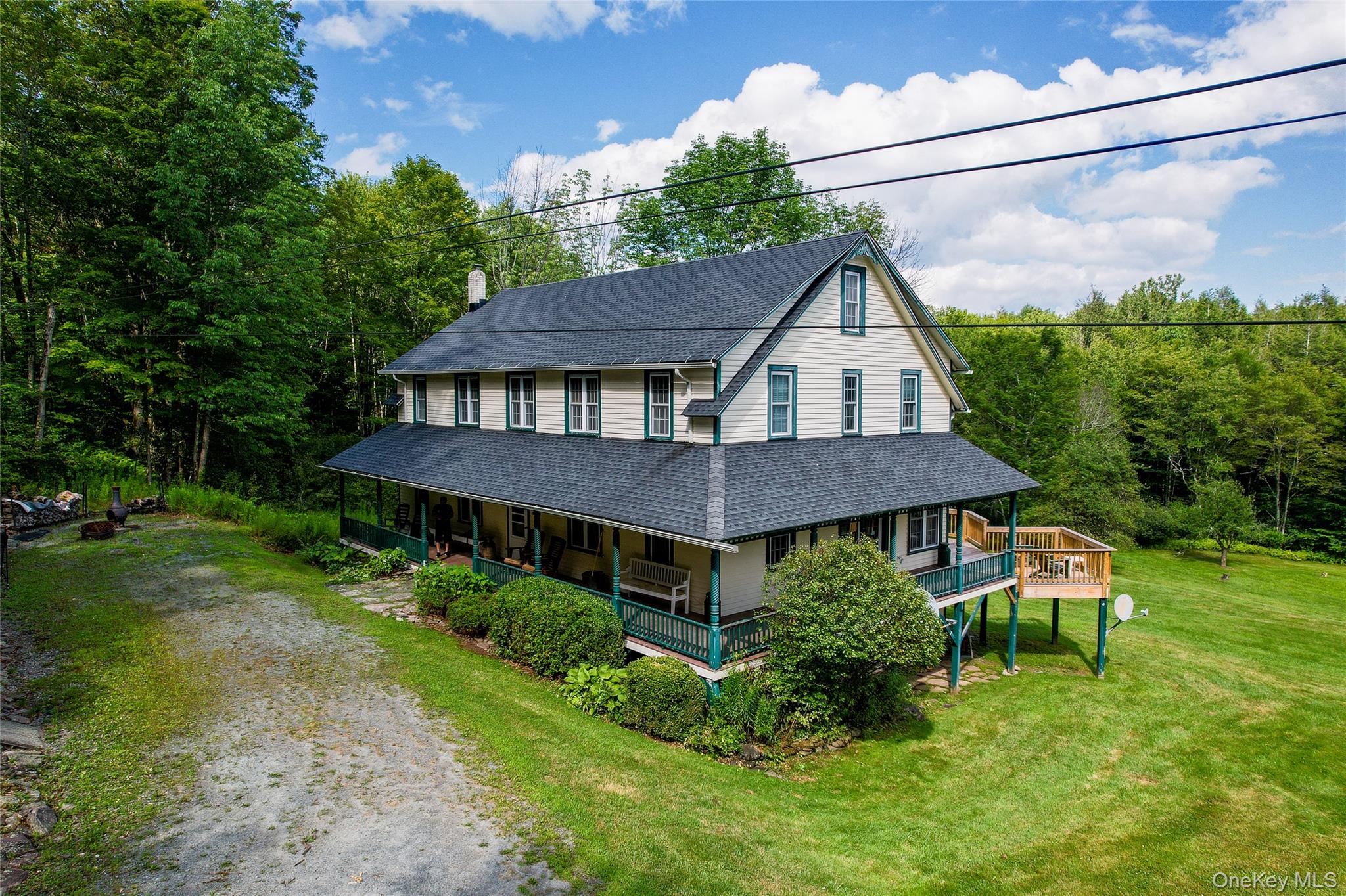 View of front facade featuring dirt driveway, roof with shingles, a front lawn, covered porch, and a forest view