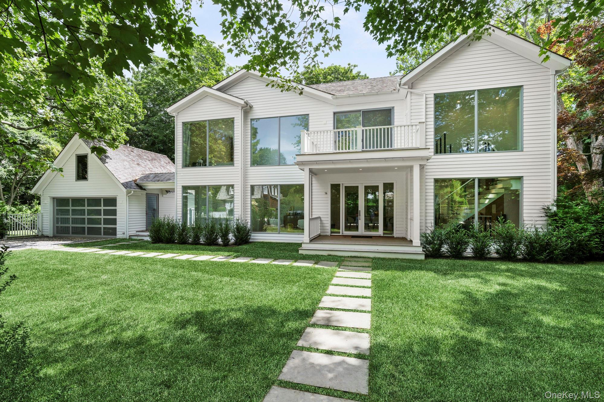 A refined new-construction residence in the heart of East Hampton Village, 16 Gould Street offers 6 bedrooms, 7.5 baths, and 4,270 square feet of thoughtfully designed living space on 0.36 acres. Built in 2025, by David Alvarado of Damar Construction, the home pairs timelessness with modern amenities and elevated craftsmanship throughout. The main level features nearly 10-foot ceilings, 6" natural white oak floors with French finish, an open foyer with direct sight lines to the covered porch and pool, and a spacious living room with a dimensional paneled wall and built-in TV-ready hookup. At the center of the home is an expansive eat-in kitchen appointed with Sub-Zero and Wolf appliances, including a six-burner natural-gas range with griddle and double ovens, Cove dishwasher, Calacatta Miraggio polished quartz countertops, custom cabinetry, and a large island with seating for ~5. Multiple sliding glass doors open to the rear deck, creating an effortless connection between the kitchen, dining area, and outdoor spaces. A first-floor ensuite bedroom, powder room, and custom mudroom with built-ins complete the level. Upstairs, the private primary suite features floor-to-ceiling windows overlooking the backyard, a sliding glass door to an expansive deck, and an open closet with dedicated his-and-hers sides. The primary bath offers a walk-in shower with both wall-mounted and handheld fixtures. Two additional bedrooms, each with built-in closets, ensuite baths, and access to the rear deck, provide comfortable accommodations for all. The finished lower level adds two additional ensuite bedrooms, both with built-in closet systems and private baths, along with a laundry room, storage, and mechanical rooms. Multiple egress windows and exterior stairs provide direct access to the backyard. Outside, the property is designed for both entertaining and easy summer living, with a heated gunite pool and built-in spa, covered Ipe decking, mature landscaping, newly installed arborvitae, full-property irrigation, and a two-car detached garage with additional storage above. A bluestone walkway leads to the front entrance, while the Belgium-block-lined driveway and gravel parking area provide ample off-street parking. Additional features include Andersen windows and sliding doors, solid wood interior doors, five-zone HVAC, natural-gas heat, central vacuum, speaker and window-shade wiring, a home alarm system, and camera-ready wiring. Just minutes from the best of East Hampton Village, 16 Gould Street offers the appeal of brand-new construction with the space, amenities, and privacy expected of a luxury Hamptons home.