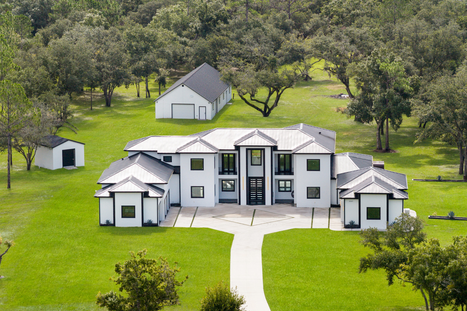 Experience exceptional privacy, craftsmanship, and contemporary luxury at this newly completed estate on 13.8 private acres in highly sought-after Panther Ridge. Positioned at the end of a quiet dead-end road, the property welcomes you through intercom-controlled gates and along an illuminated driveway to an expansive motor court with garage space for up to seven vehicles, including an APLUS 8,000-lb vehicle lift. Built with attention to quality, strength, and efficiency, the residence features two-story concrete block construction, hurricane-impact windows, spray foam insulation, zoned climate control, and a whole-house generator. Inside, soaring ceilings, designer tile flooring, custom closets, expansive windows, a sweeping curved staircase, remote-controlled electric blinds, and integrated smart-home technology create a sophisticated yet comfortable environment. Invisible Sonos-connected speakers provide seamless sound throughout. The flexible floor plan offers four spacious bedrooms, five beautifully appointed bathrooms, and two bonus rooms ideal for a home office, fitness room, media room, or additional living space. Each guest bedroom features a private bath, while the primary suite includes separate custom his-and-her closets with built-in shelving and lighting. Designed for everyday living and entertaining, the main living area features a striking dual-sided fireplace and flows into the chef-inspired kitchen. Premium Viking appliances, two ovens plus a cooktop, illuminated custom cabinetry, quartz countertops, oversized island, built-in coffee system, dedicated ice maker, and walk-in pantry create a kitchen as functional as it is impressive. Spa-inspired bathrooms feature floor-to-ceiling tile, oversized full-body showers, abundant natural light, and electric bidet toilets. Step outside to a private resort-style retreat centered around a 15' x 35' saltwater pool with dramatic waterfall fire features. Multiple finished pergolas with relaxation swings create inviting spaces to unwind, while the outdoor entertaining area features a granite summer kitchen with generous cabinetry and multiple grilling options. A private outdoor sauna further enhances the setting. For the golf enthusiast, a dedicated elevated deck is designed for practicing drives across the expansive property. Adding remarkable versatility is the approximately 30' x 80' accessory building/barn offering an air-conditioned fitness or studio space, workshop, walkable storage, an additional air-conditioned music or recreation room, kitchen and half bath on the lower level, full bath upstairs, and expansive second-floor flex space ideal for an office, game room, studio, or guest retreat. The property is further enhanced by a stocked private pond and abundant open space for recreation, equestrian use, or simply enjoying the peaceful surroundings. Panther Ridge offers approximately 22 miles of equestrian trails. Combining contemporary architecture, extensive garage and recreational space, sophisticated technology, resort-style outdoor living, and exceptional acreage and privacy, this Panther Ridge estate offers a lifestyle rarely available just minutes from Lakewood Ranch, Sarasota, premier shopping and dining, and Florida's Gulf Coast.