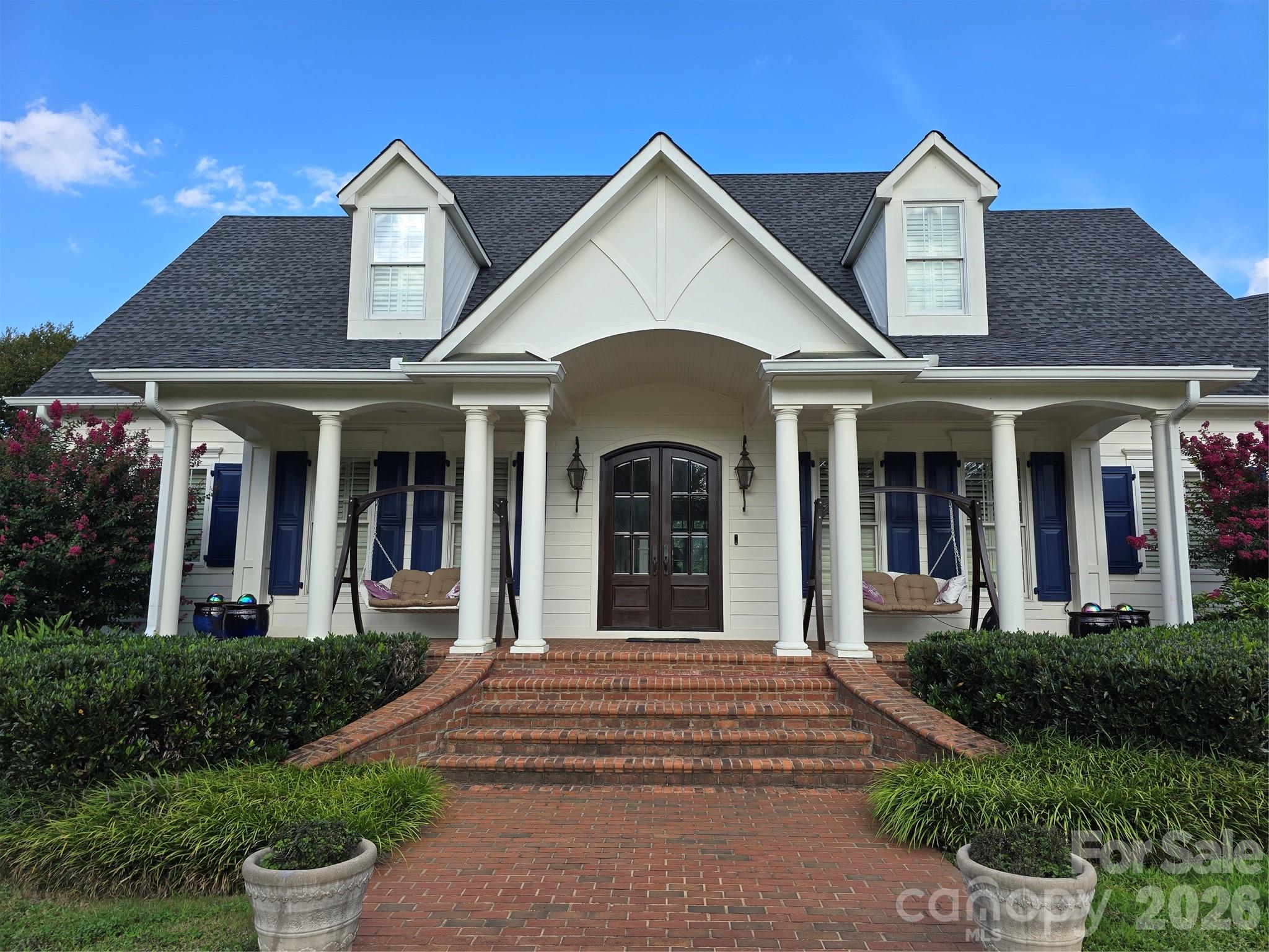 Inviting brick pavers lead to a front porch & double door entry. Inside, a spacious foyer with detailed moldings & barrel archway sets the tone. The living room boasts a coffered ceiling, stone gas-log fireplace, and built-ins. A composite deck overlooks the inground saltwater pool. The large kitchen features a granite island with sink, stainless appliances, tile backsplash, 6-burner gas range, under-cabinet lighting, and walk-in pantry. A butler's pantry connects to the elegant dining room with tray ceiling, chair rail, & wainscoting. The laundry room offers a desk & utility sink; the roomy mud room has a half bath, coat storage, and space for a second fridge. The main-level primary suite includes plantation shutters, dual vanities, walk-in closet with built-ins, custom tile shower, and water closet. Upstairs: a second primary bedroom with vaulted ceiling & en-suite, a versatile bedroom/office with en-suite, and a third bedroom with reading nook, en-suite, & large closet.