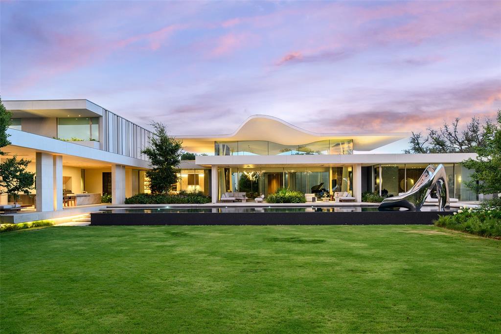 Dallas has never seen a home like Casa de Ondas. The award-winning architectural masterpiece, with over 14,000 square feet of interiors, was custom-built and conceptualized over four years, bringing together acclaimed design talent from across the globe. Marking the acclaimed international architecture firm SAOTA’s first Dallas project, this sculptural triumph rises from a verdant two-acre lot within Preston Hollow’s coveted Crespi Estate, an exclusive gated community of just four residences. Its wavy roof, inspired by surrounding tree canopies, creates a striking dialogue between architecture and nature as shifting light casts soft shadows across locally quarried limestone. Past the water lily pond, a soaring pivot door opens to a glassy hallway and dramatic double-volume living space, the heart of the home for everyday living and extraordinary entertaining. It flows to more than 5,000 square feet of covered terraces, a custom pool and spa, and lush gardens, blurring the line between indoors and out. A shimmering double-sided fireplace, sumptuous bar with an 8,000-pound marble island hand-chiseled in Italy, brass-wrapped temperature-controlled wine cellar, and chef’s kitchen with Miele appliances, designer pantry and Taj Mahal slabs elevate every gathering. The lower level reveals a hotel-quality underground speakeasy, second bar, golf simulator with privacy switch-glass views into the four-car collector’s garage, while outdoors a custom pool slide, volleyball and sport courts, outdoor kitchen and fire pit invite endless enjoyment. The main-level primary suite offers an indoor-outdoor shower, solid-stone freestanding tub, fluted fireplace and oversized Poliform closet. An expansive gym with steam room, sauna and massage room completes the wellness experience. Immersed in hand-selected plantings with no neighbor in sight, Casa de Ondas is a once-in-a-lifetime work of art where architecture, nature and extraordinary living move as one.