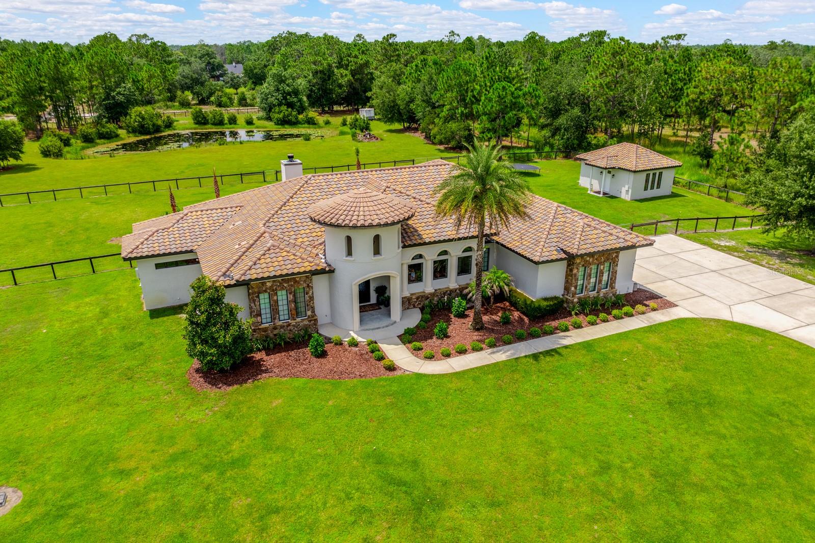 CUSTOM LUXURY, ACREAGE AND RESORT-STYLE OUTDOOR LIVING come together in this exceptional Wedgefield estate, built in 2017 and set on 3.69 fully fenced and gated acres with a stocked 1/4-acre pond, private pool and spa, and approximately 400-square-foot ADU with a full bath! Offering 5 bedrooms, 3.5 baths and 4,084 square feet of living space in the main home, this one-of-a-kind property was designed with impressive craftsmanship, energy efficiency and high-end finishes throughout. A commercial-grade gated entry leads to a striking exterior featuring a tile roof, cultured stone and natural stone accents, landscape and soffit lighting, and a custom arched steel and iron front door. Inside, vaulted ceilings with natural cypress beams make a statement in the main living area, complemented by 10’ ceilings, 8’ solid-core doors, 8” baseboards, crown molding and plantation shutters. Fully pocketing accordion-style sliders create a seamless connection to the expansive outdoor living space. The chef's kitchen delivers custom solid wood cabinetry, quartzite countertops, a Wolf gas range, Sub-Zero refrigerator, built-in ice maker, main sink and separate prep sink. The primary suite is equally impressive with a custom walk-in closet featuring built-in shelving and a center island. A flex room is already plumbed for an additional bathroom, adding even more versatility. Outside, enjoy a tongue-and-groove lanai ceiling, wood-burning fireplace, outdoor kitchen with grill, beverage refrigerator and sink, remote-controlled retractable screen, and a pool and spa surrounded by an exposed aggregate deck. The acreage is fully fenced with additional cross fencing, while the stocked pond and detached ADU expand the possibilities for this unique property. Quality construction includes spray foam insulation in the exterior walls, ceilings and attic, insulated interior walls, an insulated garage door, solid concrete pantry/safe room, owner-owned 500-gallon underground gas tank, two A/C systems, three tankless gas water heaters, Generac backup generator, hardwired alarm and exterior security camera system, and built-in surround sound. Located in Orlando's desirable 32833 ZIP code, Wedgefield is known for spacious properties, natural surroundings and abundant wildlife, with the Hal Scott Preserve nearby. Zoned for A-rated Wedgefield K-8 and convenient to Wedgefield Golf Club, Wedgefield Park, FL-520, SR-50 and SR-528, with easy access to Waterford Lakes Town Center, UCF, shopping and dining. A rare opportunity to own a custom luxury pool home where privacy, acreage and exceptional amenities are all part of everyday living. SELLER FINANCING IS AVAILABLE TO QUALIFIED BUYERS. Call today to schedule your private tour!