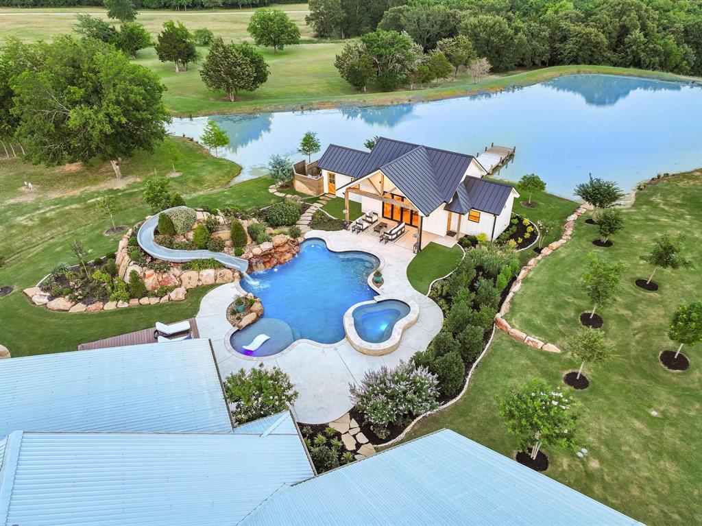 Absolutely stunning resort-style estate just minutes from Lake Texoma, offering the flexibility to live full time, enjoy as a turn-key second home, or operate as a premium short-term rental retreat. In 2023, the owners invested over $1m in enhancements, including a new luxury pool house, heated garage-shop, resort-style pool with slide and waterfalls, expanded pond and dock, and sophisticated landscape design that compliments the natural beauty of the 10-acre setting. The main residence received a complete interior and exterior refresh, elevating the design to a polished, luxury aesthetic. Set on just over 10 manicured acres with a private stocked pond and sweeping country views, the 6000+ SF residence features 5 bedrooms, 4.5 baths, and an expansive open living and dining space ideal for entertaining large groups. The gourmet kitchen showcases commercial-grade stainless appliances, double ovens, pot filler, oversized island, and a generous walk-in pantry. The primary suite offers direct access to a private porch plus a spa-inspired bath with large walk-in shower and custom closet, while the upstairs bunk room and media room create an ideal separate space for guests or rental parties. Outside, enjoy true private-resort living with a heated gunite pool and spa, rock waterfalls, waterslide, outdoor shower, fire pit, and multiple covered patios designed for year-round indoor-outdoor living. The beautifully finished pool house adds a full kitchen, living area, and full bath, opening to the pond and dock for fishing, paddleboarding, or quiet sunset views. Extensive parking includes a circular drive, porte cochere, multiple carports, and a large heated garage with 12-foot doors, ideal for RV or boat storage, car collection, or even an indoor pickleball court. Modern comforts such as dual laundry areas, safe room, dog wash, smart-home capabilities, and high-speed internet wiring support effortless everyday living or hands-off remote management as a short-term rental.
