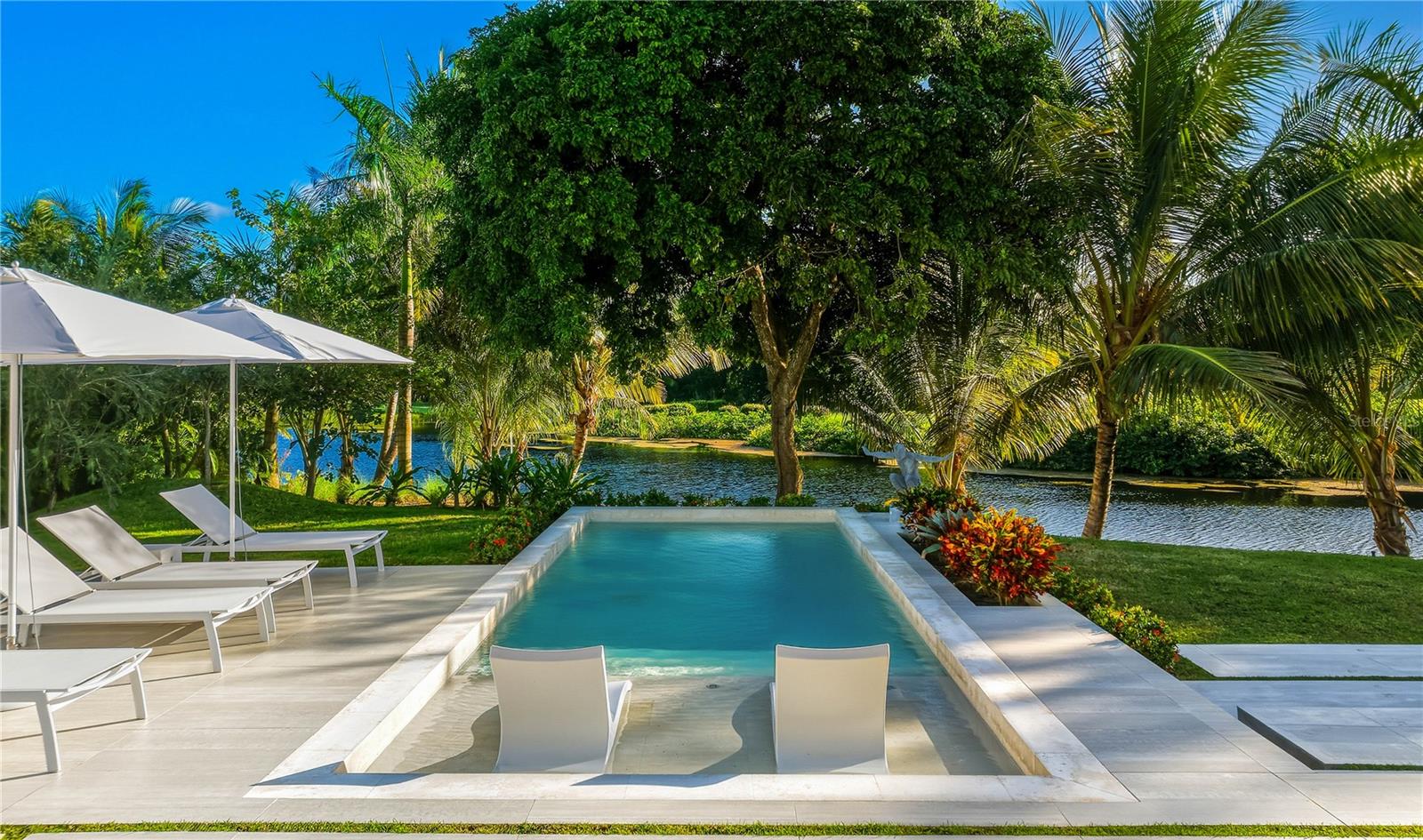 No expense spared on this true to form Caribbean contemporary new construction, sitting blissfully at the eastern entrance to the rainforest and within the esteemed enclave of the branded Four Seasons Resort and Residences Puerto Rico in Rio Grande. Completed in 2024, 23 Las Estancias stands a testament in true adoration to architectural intention and sophisticated purposeful interior design. Sitting on just over 1/2 acre, each curated detail resonates throughout this 3 bedroom, 3 full bath and 2 partial bathroom single level estate. 20+ Ft entry ceilings pull all of the natural light from the floor to ceiling glass doors, with  broad facing western exposure to the lake, mountains and lush tropical backdrop that only the El Yunque rainforest can afford. Brushed blond wood palettes delicately accent the pinnacle of each room's ceilings, pulling in natural textures to the all concrete structure. Limestone floors add a cool tonality to the juxtaposition of ultra green foliage enveloping the home's elevated exterior facade landscaping. Cascading honed marble countertops highlight this double sized gourmet kitchen, featuring a gratuitous 19x19 footprint, and cornered by 10+ ft glass doors that open fully to the property’s magical oasis. Privacy and purpose reign here, where your outdoor summer kitchen equipped with full gas range, sink and bar moves fluidity towards your zero edge swimming pool, which is adjacent to your outdoor shower and bath, dining, sunning areas and hidden entertaining spaces. Guest suites, each highlighting the exotic nature of living within the resort, feature walk-in closets, ensuite baths and full length picture windows encasing the spaces with fresh sunkissed natural light. The primary wing serves as an homage to refined peace. Double entry doors swing inwards towards the 4 post california king bed, masterfully angled towards the estate’s western outdoor living, where hints of running water from the lake abutting the property’s line, and coconut bearing palms sway off in the distance, to this coast's constant melodic breezes. A basin tub swathed in the greenery exposed by the large bay windows, and indoor/outdoor shower textured in raw stone elements, and an 11' 11” X 13' 11” temperature controlled boudoir and closet round out the home's impeccable design. Warm neutrals kiss every element of design here, where Lutron lighting and shades throughout, a fully off grid solar installation on roof and numerous other refined details, allow the owner the ease of purposeful living. 23 Las Estancias serves as a culmination of vision and passion elegantly aligned in both presence and form. The only of its kind, a true 1 of 1.