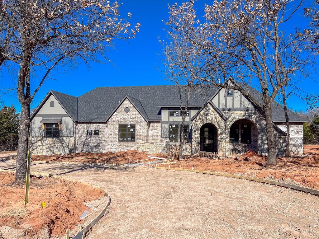 Experience the perfect blend of luxury, comfort, and privacy in this stunning English Tudor–style home, ideally situated on a one-acre, heavily wooded homesite within a gated community and the highly sought-after Edmond Public Schools district. Thoughtfully designed with all living spaces on one level, this home offers 4 bedrooms, 3.5 bathrooms, a private study, and an inviting game room. The heart of the home is the chef’s kitchen, featuring double islands, a granite composite sink, quartz backsplash, double ovens, and a spacious walk-in pantry—perfect for everyday living and entertaining alike. The adjacent dining area is accented by a striking stone feature wall, adding warmth and character. The living room showcases a beautiful stone fireplace and a dramatic 16-foot sliding glass door that opens to the expansive patio, seamlessly connecting indoor and outdoor living. Step outside to enjoy the large covered patio complete with a motorized screen, built-in grill, and outdoor fireplace—ideal for year-round entertaining. The private study is a true retreat, highlighted by custom library bookcase shelving with a sliding ladder and soaring 14-foot ceilings. The game room offers additional space to unwind, featuring an arched built-in bar and decorative ceiling beams on the vaulted ceiling! Gorgeous site-finished wood floors flow throughout the main living areas and into the vaulted primary suite, which boasts wood beams, separate vanities, a freestanding soaking tub, an oversized walk-in shower, and two spacious walk-in closets. Additional highlights include a 3-car insulated garage with modern glass doors and in-ground storm shelter, a circular driveway, and exceptional craftsmanship throughout. Offering serene wooded views and upscale finishes, this remarkable property provides a rare opportunity to enjoy refined living in a private, gated Edmond community!