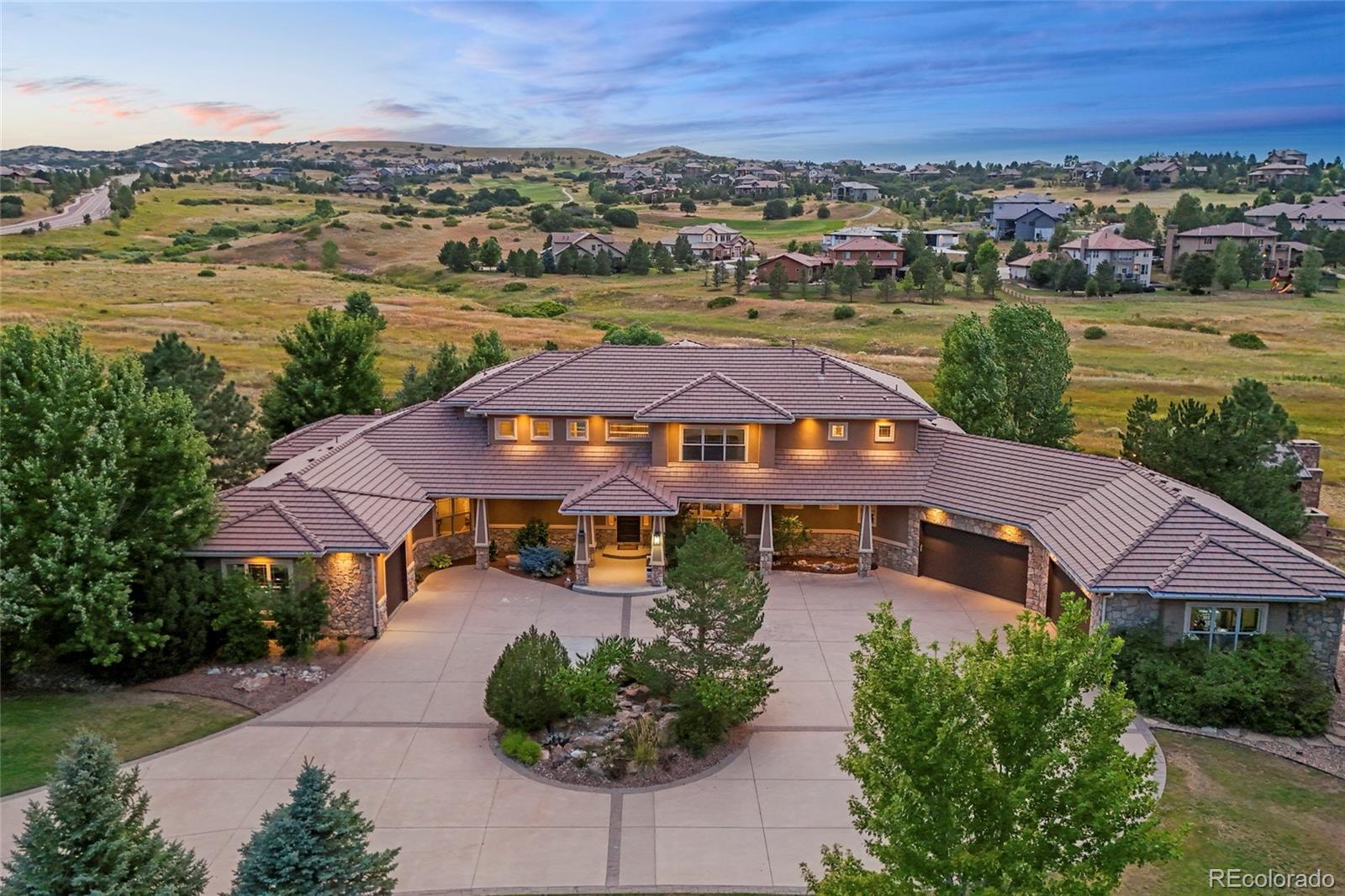 Experience elevated living at 5625 Twilight Way, a remarkable retreat within the prestigious private golf club community of Pradera. Set on nearly two acres and backing to open space, this exceptional property offers rare privacy, sweeping views, and unforgettable Colorado sunsets.From the moment you arrive, the home impresses with refined warmth and timeless elegance. Rich wood accents, expansive sun-filled windows, and thoughtfully crafted custom details are showcased throughout. A grand foyer with a striking spiral staircase opens to the great room, where stone-accented walls, a cozy fireplace, and dramatic west-facing windows create a stunning focal point. The space flows seamlessly into an elegant dining room with tray ceilings and a butler’s pantry—ideal for hosting.The chef’s kitchen blends beauty and function with custom cabinetry, high-end appliances, and an oversized island topped with white quartz countertops, perfect for everyday living and entertaining. The main-level primary suite is a true retreat, featuring a double-sided fireplace, heated floors, private deck access, a custom walk-in closet, and a spa-inspired bathroom. An additional main-floor bedroom with an en-suite bath offers flexibility for guests or multi-generational living.Downstairs, enjoy an entertainer’s haven complete with a second kitchen, stylish bar, home theater, game room with fireplace, and a dedicated wine cellar and tasting room. Outside, multiple outdoor living spaces invite you to relax and take in Colorado’s natural beauty.An impressive five-car garage provides ample room for vehicles, storage, toys, and a golf cart. A grand circular drive enhances the sense of arrival. This extraordinary home must be experienced in person to fully appreciate its comfort, craftsmanship, and captivating charm.