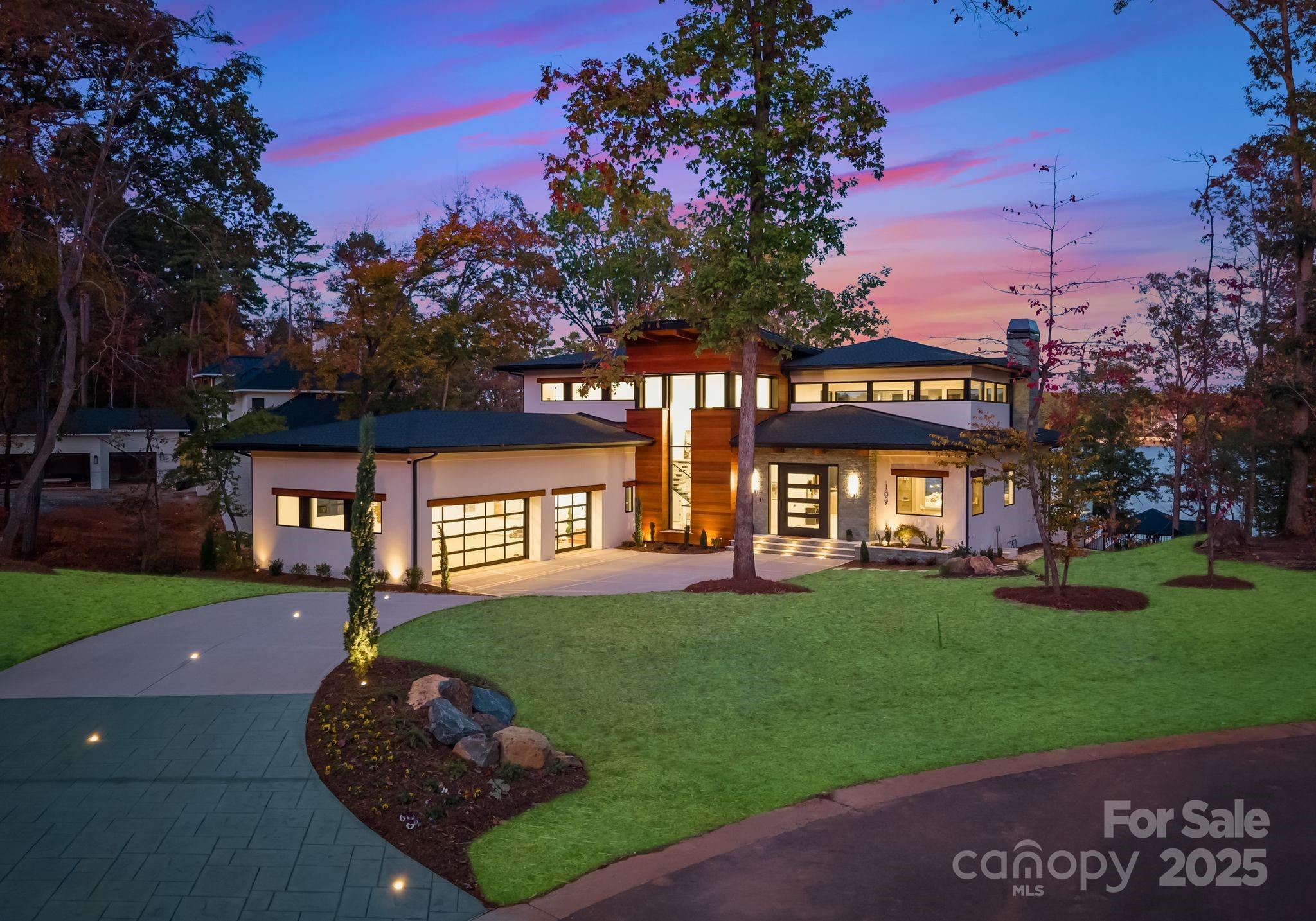 Exquisite Waterfront Masterpiece on Lake Tillery – Discover an architectural work of art on the shores of Lake Tillery. Designed and built by Artistic Contractors, one of Charlotte’s premier design/build firms, this 7,940 sq ft modern lakefront retreat embodies warmth, innovation, and serenity. Set on nearly an acre of gently sloping land beneath mature trees, this property blends natural materials with bold geometry to create one of the most extraordinary residences in the Carolinas.
Homes in the sought-after Edgewater community have consistently sold above $600 per sq ft since 2022, with a neighboring property closing in August 2025 at $672 per sq ft. Priced at only ~$660 per sq ft, this fully loaded lakefront showpiece offers unmatched design and luxury—an exceptional value for a home of this caliber.
Step through the monumental 10’ x 10’ pivot door and into the breathtaking 1,400 sq ft atrium great room—a soaring, light-filled space combining living, kitchen, and dining under a 28-foot pyramidal clerestory ceiling clad in rich imported Peruvian Cumaru wood. Supported by striking exposed steel beams, the atrium provides a grand opening through a 24-foot folding glass wall to covered terraces. This room stands among the largest and most architecturally striking private spaces in the Carolinas.
Throughout the 6-bedroom, 5.2-bath residence, form and function meet effortlessly. The chef’s kitchen features a 10’ x 6’ waterfall island, professional Monogram appliances, Miele induction cooktop, and concealed scullery. The great room’s Dimplex 74” linear fireplace anchors a dramatic wall of book-matched soft stone and carved wood panels. The floating mono-stringer staircase with glass railing and 3” white oak treads rises like a sculpture.
The primary suite is a sanctuary of peace with floor-to-ceiling glass windows offering panoramic lake views. The spa-inspired bath features a freestanding tub, 24” rain shower over a Cumaru deck floor, and spacious his-and-hers closets with custom cabinetry and ambient LED lighting.
Outdoor living exceeds expectation: over 1,700 sq ft of covered decks and terraces finished with Cumaru ceilings and imported Indonesian white Palimanan Limestone floors.  Glass railings, ceiling fans, built-in speakers, and motorized screens differentiate the outdoor living from any competition. A resort-style saltwater infinity pool and spa clad in Indonesian Sukabumi stone glows in deep lagoon hues, surrounded by matching stone planters and Palimanan limestone decking. The outdoor kitchen includes a Coyote 42” grill, Cumaru hood, sink, and cabinetry for effortless entertaining.
The property’s private 1,200 sq ft dock offers two covered boat slips and a covered entertainment area overlooking the long-range views of Lake Tillery.
Additional features include all-aluminum thermally broken windows and doors with Low-E argon-filled glass, open-cell foam insulation, tankless hot water, smart surveillance and lighting systems, 200+ LED recessed can lights, and an EV-ready three-car garage. An underground irrigation system pumps directly from the lake to keep the landscape lush year-round.
Every element—wood, steel, stone, and glass—was selected for beauty, durability, and emotional resonance. This is not just a house; it’s a sanctuary designed to inspire joy, peace, and creativity. Experience the art of living at 109 Tidewater Court—an extraordinary waterfront retreat where design and nature meet.