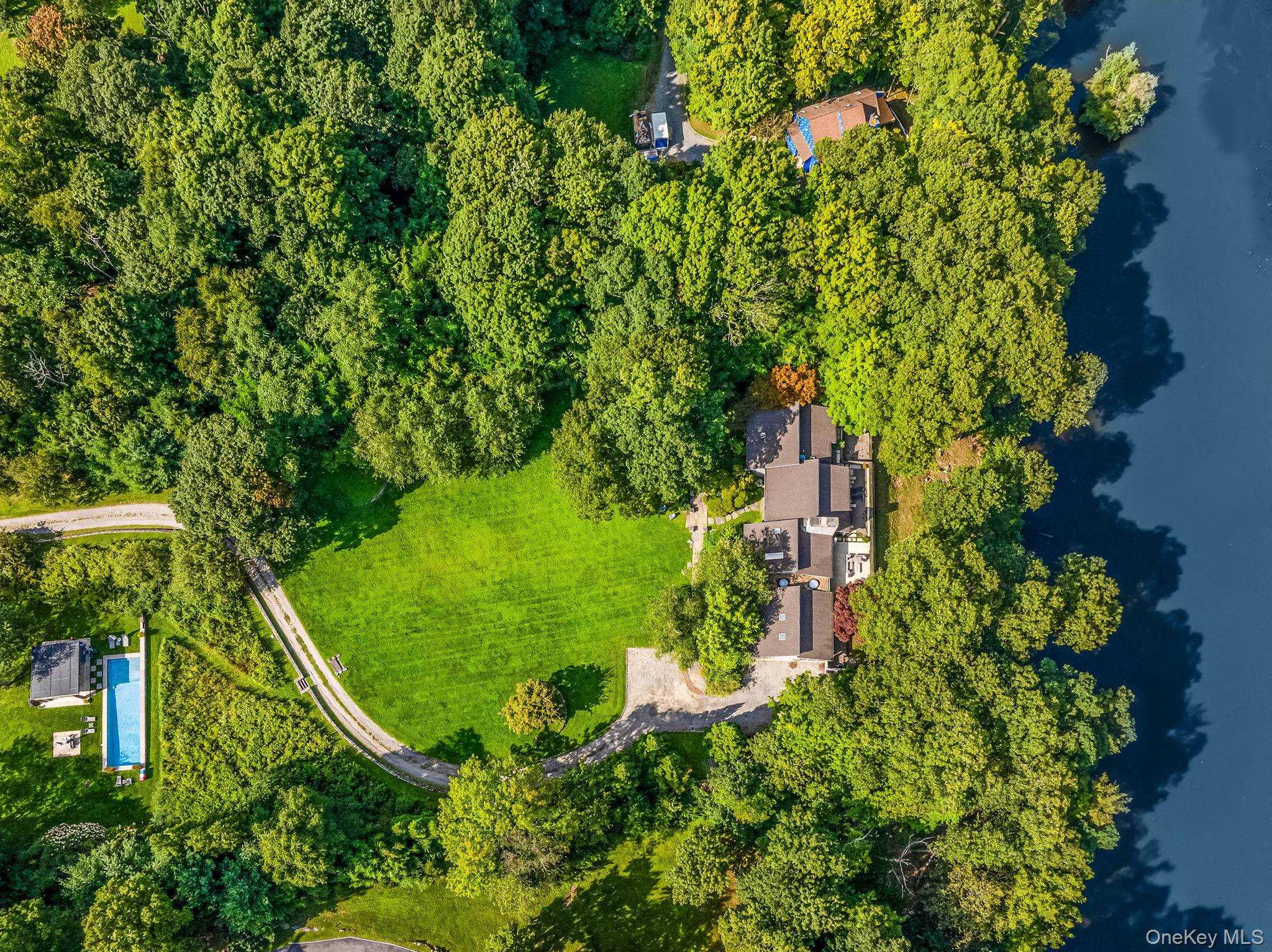 Experience the art of living well in this extraordinary private retreat overlooking Heaptaugua Lake. Set on just under five acres, the property offers total serenity while remaining just minutes from Chappaqua’s quaint downtown, restaurants, Metro-North, and shopping. Enter through the gates and follow the sweeping driveway as it curves past the pool house and pool, passing a sweeping lawn before reaching the main residence. This sophisticated one-level contemporary is deceptively understated from the front yet opens dramatically in the rear with walls of glass and lofted ceilings framing breathtaking views of mature trees and shimmering water. Multiple living spaces flow effortlessly to expansive terraces, anchored by a striking double-sided stone fireplace serving both the living and dining rooms. The private bedroom wing includes three bedrooms, highlighted by a serene primary suite with a stunning spa-like bath, while a separate fourth bedroom and family room on the opposite side of the home create the perfect guest quarters. An art lover's dream with gallery style hallways perfect for showcasing a collector's treasured works. A chef’s kitchen completes the offering with custom Italian cabinets by Schiffini, creating an intimate space for meals yet perfect for entertaining. Rarely does a property of this caliber and setting become available—an exceptional opportunity awaits.