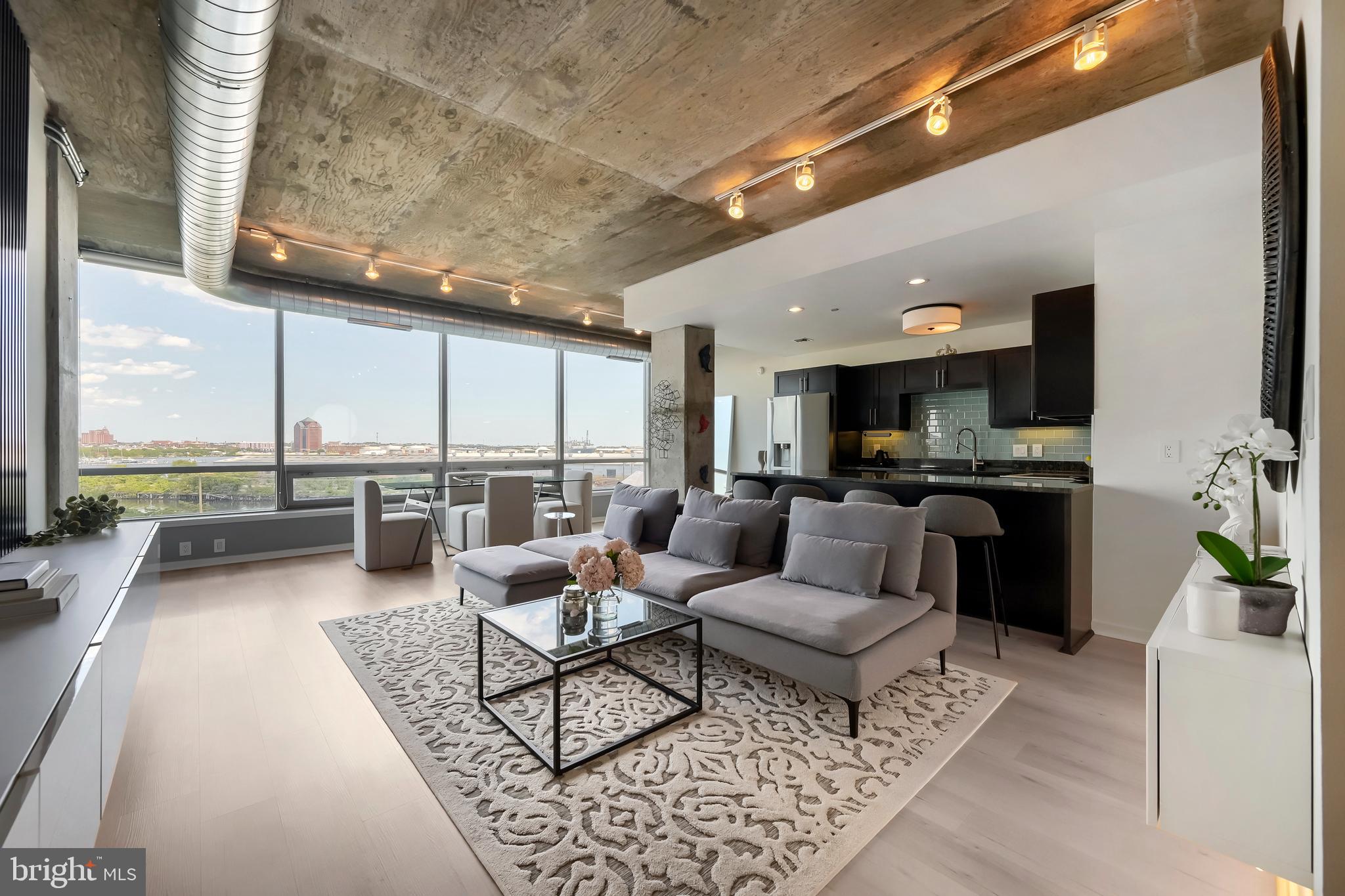 Stunning panoramic views of the Baltimore Harbor and Patapsco River frame this beautifully updated, rarely available one-bedroom, one-and-a-half-bath residence at Silo Point. Bathed in natural light from its sought-after eastern exposure, Residence 514 offers an expansive open floor plan where dramatic walls of glass capture sweeping water vistas from nearly every room. Blending modern luxury with the building’s iconic industrial architecture, this sophisticated home features soaring ceilings, exposed concrete details, and luxury vinyl plank flooring throughout, creating a refined yet contemporary aesthetic. A gracious entry opens to an expansive great room designed for both effortless entertaining and comfortable daily living. The open-concept kitchen is anchored by an island with seating, sleek cabinetry, stainless steel appliances, and abundant storage, seamlessly connecting the kitchen, dining, and living areas. Custom built-in media cabinetry enhances the living room, while Lutron shades provide convenience and privacy. Just beyond, a private balcony extends the living space outdoors, offering a front-row seat to spectacular sunrises and waterfront views. The generously proportioned primary suite is a tranquil retreat featuring automated window treatments, a spacious walk-in closet, and additional linen storage. The spa-inspired en-suite bath is appointed with a double vanity, soaking tub, and separate walk-in shower. A stylish powder room, oversized laundry room with a full-size stacked washer and dryer, and custom storage solutions further enhance the home’s functionality and appeal. Included with the residence are two deeded garage parking spaces. Experience the coveted Silo Point lifestyle with an impressive collection of full-service amenities, including a 24-hour front desk attendant, on-site management, a state-of-the-art fitness center with yoga studio and treatment room, boardroom, game room, EV charging, and the spectacular 19th-floor Sky Lounge with sweeping harbor and city views. Perfectly situated in the heart of Locust Point, residents enjoy walkable access to waterfront parks, acclaimed dining, neighborhood favorites, the water taxi, and convenient access to I-95. This is waterfront luxury living at its finest.