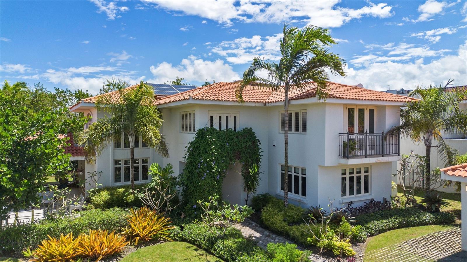 Near Dorado Beach East's south entrance, this two-story residence sits on a 1,400 square meter lot with approximately 5,100 square feet of living space across four bedrooms, maid's quarters, six full bathrooms, and one half bath. Double-height ceilings and expansive windows draw natural light through the main living areas, connecting formal and informal spaces suited to daily life and larger gatherings. The kitchen, dining, and living areas flow without interruption, while outdoor terraces and mature landscaping provide a private setting beyond the main rooms. Infrastructure built for self-sufficiency includes a solar panel system with battery backup, a full diesel generator, and a 1,200-gallon water cistern. In well-maintained original condition, the home presents a clear path toward customization or modernization for a buyer ready to put their mark on one of Puerto Rico's most established private communities.