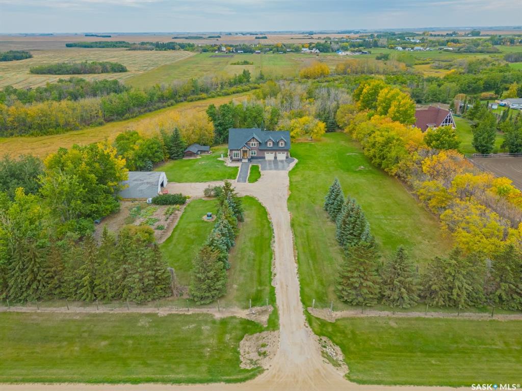 Hidden among mature trees just minutes north of Osler, this custom-built Pawluk Homes property feels more like a private country estate than a typical acreage. Groomed trails wind through the property, fruit trees are scattered throughout, page-wire fencing surrounds the grounds, and a natural coulee along the back creates a landscape that feels established, secluded and completely removed from subdivision living. The home itself was built on a grand scale, but with a floor plan that is anything but ordinary. The main level is open, warm and architectural, with hardwood and tile flooring, a gas fireplace and open railing that connects the spaces without losing definition. Then there’s the primary suite — unusually and thoughtfully located on the main floor. It features a substantial walk-in closet and five-piece ensuite with dual sinks, corner jetted tub and tiled shower. Upstairs is where this home really breaks away from the expected. Two bedrooms and a four-piece bath are joined by an incredible bonus room measuring over 600 sq. ft. — a space large enough to completely reinvent depending on how you live. The walkout basement adds even more potential, with nine-foot ceilings, in-floor heat, two bedrooms already framed and a bathroom roughed in. There’s also a chicken coop, storage shed, numerous fruit trees and groomed trails that make the acreage feel as usable as it is beautiful. Central AC, public waterline, a mound septic, in-floor heat, and the craftsmanship of a custom Pawluk Homes build round out a property that was clearly designed with both comfort and longevity in mind. This isn’t about moving farther away. It’s about having more — more privacy, more space, more flexibility and more room to create the kind of life that simply doesn’t fit inside city limits.
