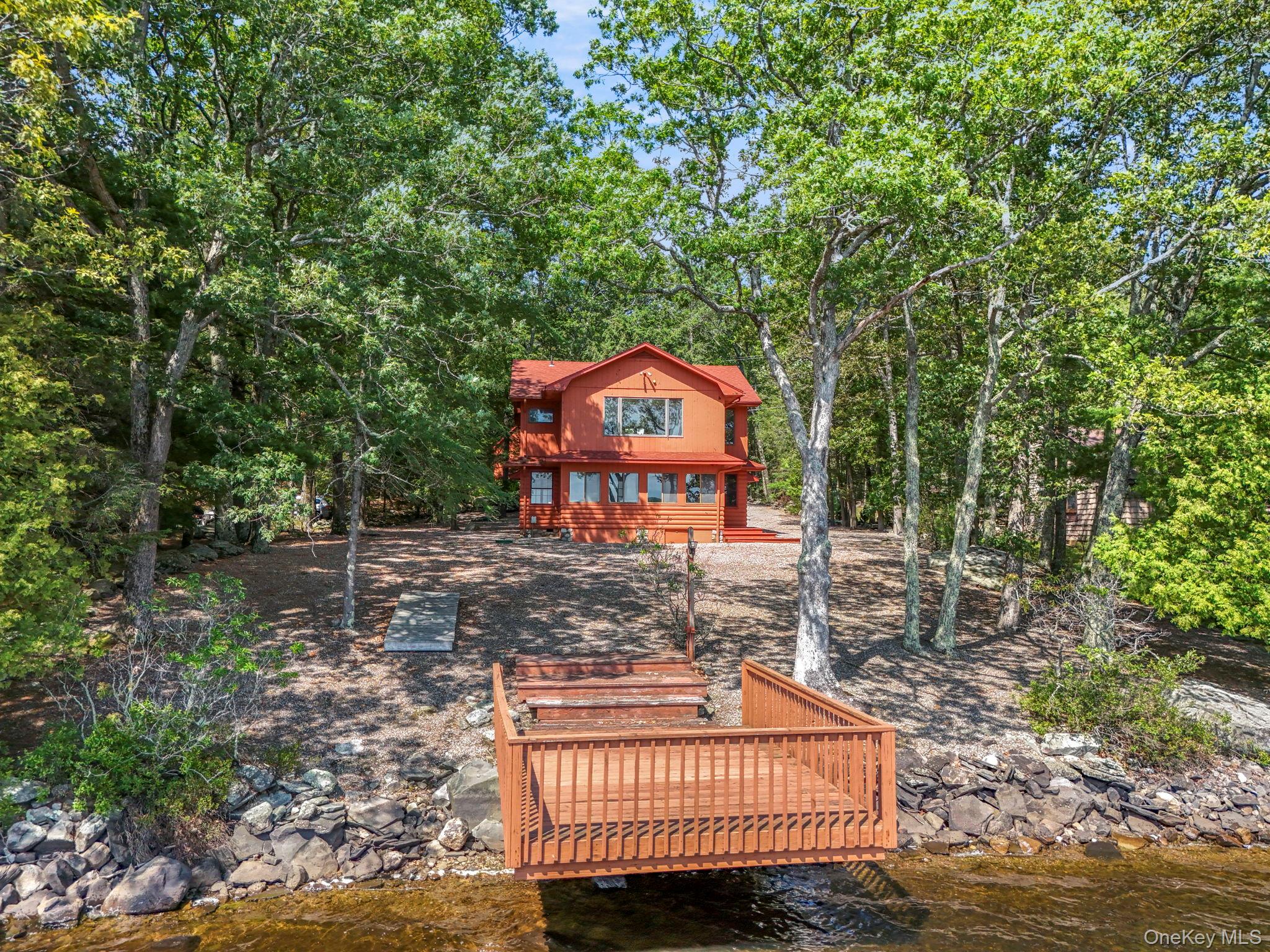 Some properties in Wolf Lake carry history. 194 Canal Road carries it well.The original 1940s cabin anchors the home in an era when lake life was simpler and the details were built to last, aged pine paneling with a warm golden tone, original window hardware, and a stone fireplace that has anchored this room for eighty years. A soapstone wood-burning stove, added with the same care, extends that tradition. A subsequent addition brought the home to four bedrooms and two full baths, and delivers a commanding lake view from the primary suite that is difficult to overstate.But the location is the real story.Gravel waterfront extending to the water's edge is exceptionally rare in Wolf Lake, where community regulations prohibit it on every other parcel. This property carries grandfathered status; you could not replicate it. The cantilevered dock sits at the end of a clean sight line from the house, with full southern exposure across the water. Morning coffee on the dock. Wine at sunset. Neither requires imagination here.A three-year-old septic system, new appliances, and an oversized two-car garage with a staircase to a generous loft suitable for a workshop or studio round out a property that is structurally sound where it counts.Wolf Lake is one of Sullivan County's most sought-after private lake communities, featuring 1,800 acres of protected forestland, three spring-fed lakes, a community beach, miles of hiking trails, and a clubhouse with a full calendar of events, kayaking, paddleboarding, sailing, pickleball, blueberry picking, and seasonal socials among them. Just 90 minutes from the George Washington Bridge. One-time membership fee: $5,250. Annual dues: $1,350.