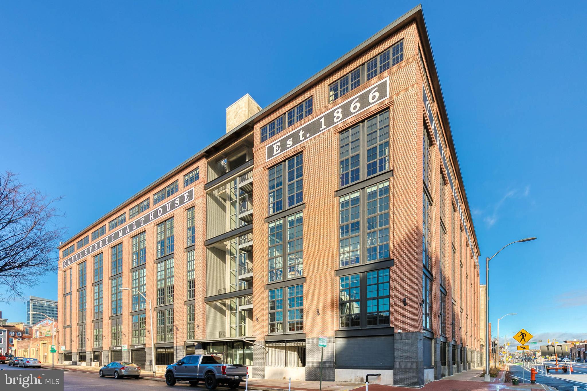 Experience elevated city living in the heart of Baltimore’s iconic Little Italy neighborhood, where timeless character and modern luxury blend seamlessly. Set within a beautifully preserved historic building, this exceptional residence offers the rare convenience of secure garage parking and elevator access directly to the fourth floor, where your home overlooks a charming community green space below. From the moment you step inside, you’re greeted by an expansive, light-filled open floor plan designed to impress. A dramatic wall of oversized windows frames sweeping city views while bathing the space in natural light, creating an airy, sophisticated ambiance perfect for both everyday living and upscale entertaining.  The gourmet kitchen is a true showpiece, crafted for the culinary enthusiast and the entertainer alike. Outfitted with high-end stainless steel appliances, a striking oversized center island, a sleek range hood, and rich shaker-style espresso cabinetry, it effortlessly combines style and function. A custom pantry complete with a built-in wine and beverage refrigerator adds both convenience and elegance, ensuring everything you need is at your fingertips. The entire main level flows seamlessly, offering an ideal layout for hosting gatherings or enjoying quiet evenings at home. A generously sized bedroom and beautifully appointed full bath with custom tile work provide flexibility for guests or additional living space, while abundant closet storage enhances everyday practicality.  Upstairs, a thoughtfully designed second level offers even more versatility, including a comfortable den and a dedicated office space ideal for working from home or creating a private retreat. The expansive primary suite is a sanctuary unto itself, featuring a massive walk-in closet and a spa-inspired en suite bath adorned with marble tile, a double vanity, a separate glass-enclosed shower, and a luxurious soaking tub designed for relaxation. Step out onto your private balcony to savor your morning coffee as the city comes to life, then enjoy the unmatched convenience of walking to Baltimore’s finest dining, cafés, and waterfront attractions. This is refined urban living at its absolute best.