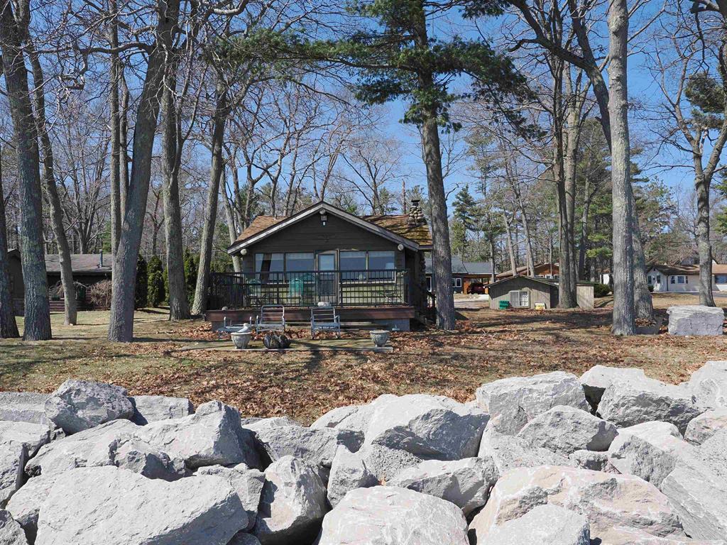 This classic Lake Huron log cottage is warm, cozy, and inviting-just like the traditional cottages we remember from our youth. The property includes a double lot with 100 feet of south-by-southeast frontage, offering beautiful sunrises over the big lake. A vacant lot across the road is also included, providing space for extra parking or the potential to build a guest house or garage.  The cabin retains its original charm, centered around a beautiful stone fireplace in the living room. Despite its rustic feel, it features full plumbing and central heat, allowing for comfortable year-round use. The two lots and the lakeside deck provide ample space for outdoor activities.  The 100 feet of frontage has been reinforced with a riprap seawall, and the sandy, shallow lake bottom beyond it makes for excellent swimming and water sports. If desired, the property could also serve as a great building site for a new home.  There is a guest house on the property, though it is in questionable condition. The cabin is conveniently located just off US-23 for easy access, and the vacant lot extends from US-23 to the cabin-allowing for a potential drive-through layout if desired.