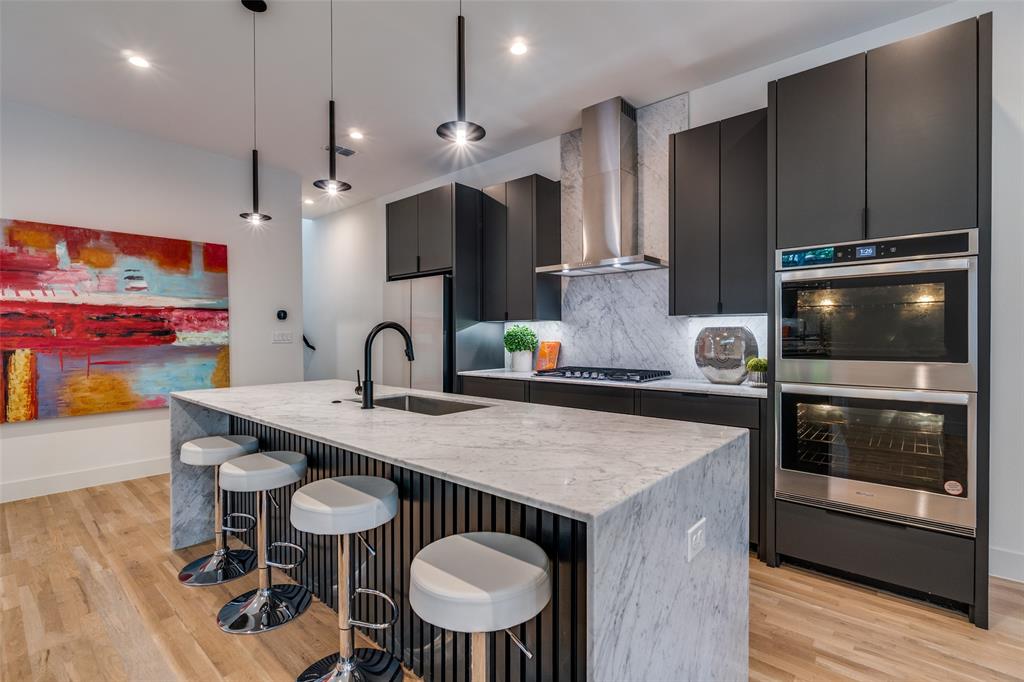 Kitchen with a breakfast bar area, a center island with sink, backsplash, light stone countertops, and appliances with stainless steel finishes