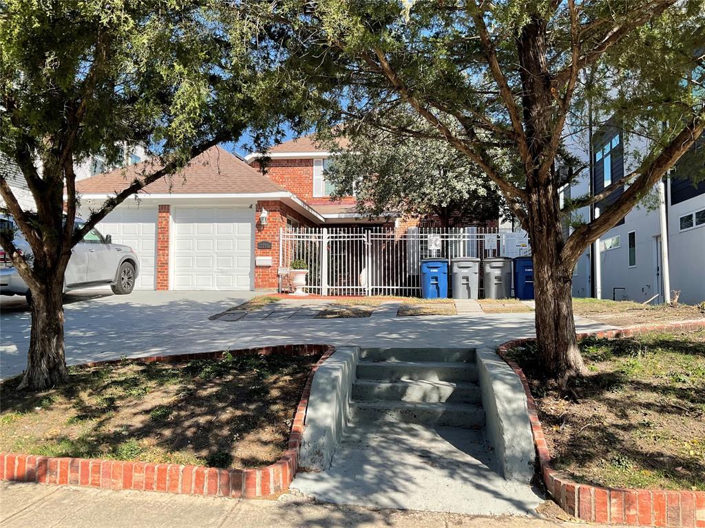 View of property hidden behind natural elements featuring brick siding, concrete driveway, and roof with shingles