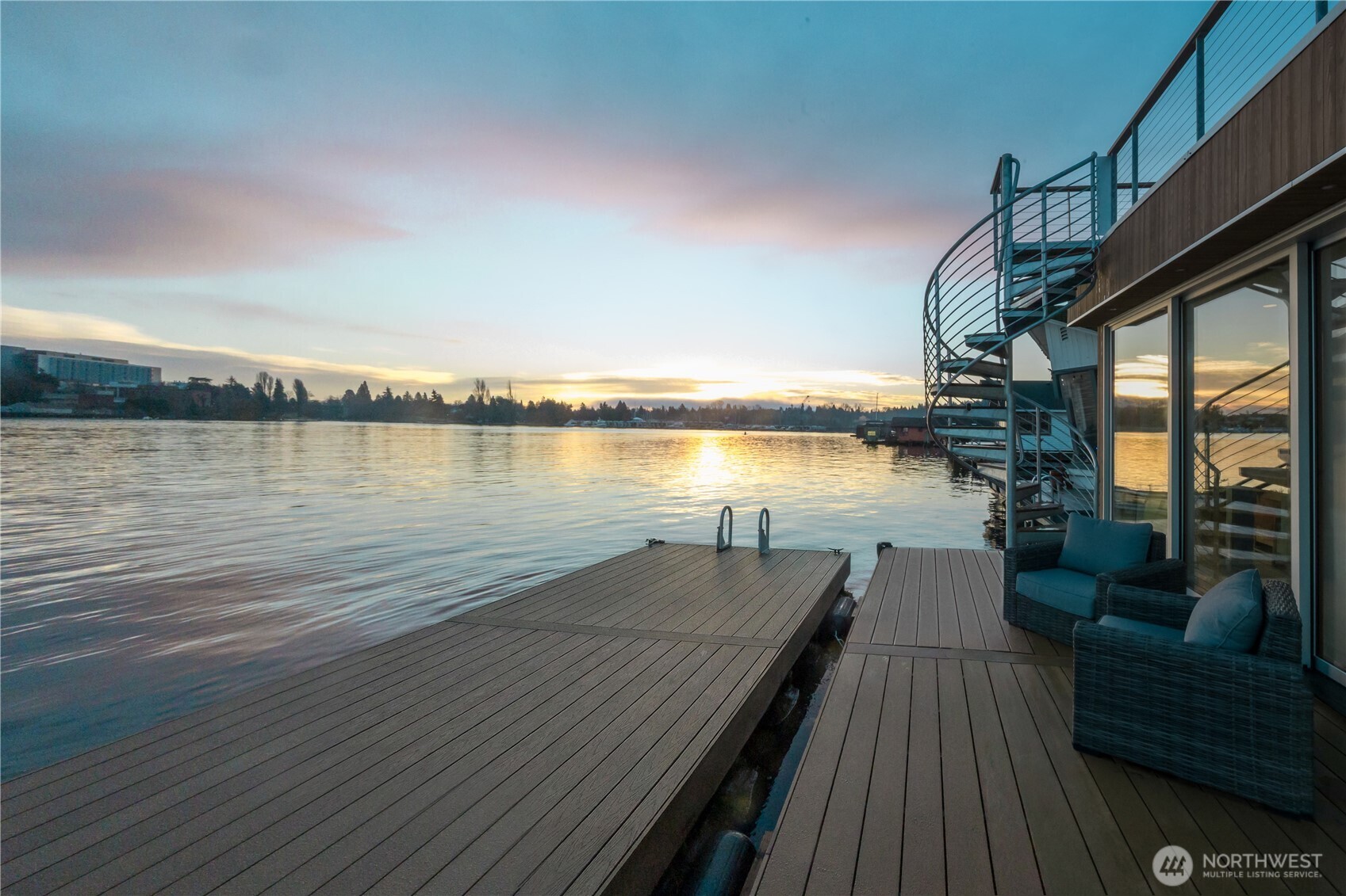 Newly constructed and expertly built by Lithic Construction, this floating home embodies quiet sophistication from its premier end-of-dock setting on Portage Bay. A warm modern aesthetic highlights sweeping 180-degree views and seamless indoor–outdoor living through a 20-foot, floor-to-ceiling sliding door system. Daltile polished quartz countertops in white sand, induction range, large center island, and seating for four.  Heat pump for controlled temperature in every room.  Auto shades for complete privacy.  Two bedrooms and two bathrooms. The primary suite features 14’ vaulted ceilings and an ensuite bath. A rooftop deck, front patio, and auxiliary raft provide approximately 950 sqft of outdoor living. Includes rare 28’ separately boat moorage + two parking spaces. Natural cedar siding is paired with custom steel railings and a striking staircase.  Experience the best of the Located minutes from 520 to head to the east side, I-5 for traveling north/south, and multiple bike trails.  This is Pacific Northwest living in a waterfront sanctuary.