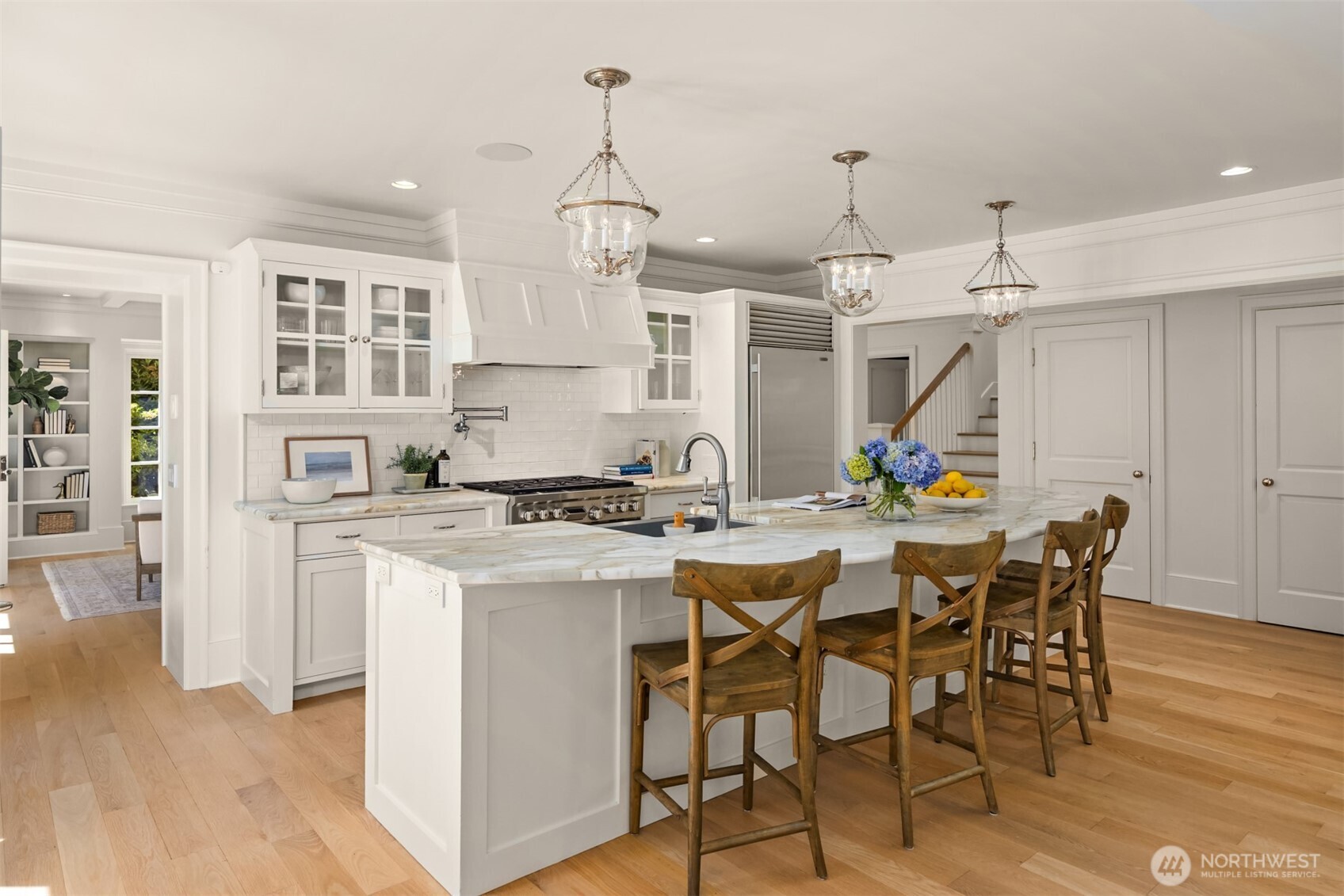 Elegant white kitchen featuring a marble-topped island and glass-front cabinetry.