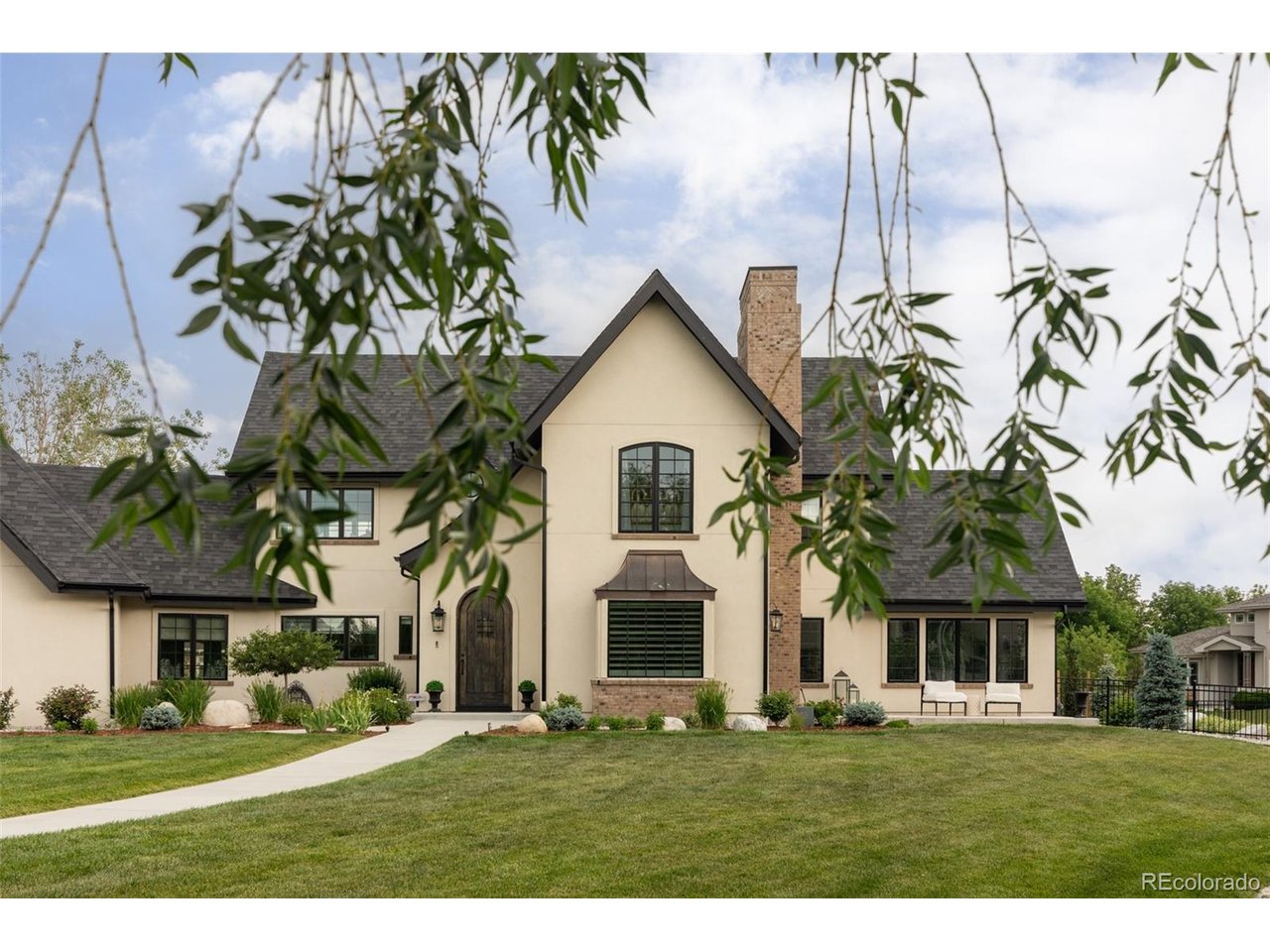 A rare Colorado lakefront retreat, this custom Tudor Revival offers private lake access, serene water views, and a resort-style backyard setting that is exceptionally hard to find. Built in 2022 and designed with the impeccable eye of an interior designer, the home blends timeless architecture with refined, curated finishes.Created for elevated everyday living and unforgettable entertaining, the outdoor spaces include a pool and integrated spa with four fountains, LED lighting, and a retractable locking safety cover, all overlooking the lake. Multiple patios create seamless indoor-outdoor living, including a covered patio off the great room, kitchen patio, and charming colonnade near the mudroom and garage. Landscaped grounds feature garden retaining walls, irrigation/drip systems, improved drainage to the lake, 5' iron fencing with three gates, and direct access to the neighborhood garden and bridge. Inside, wide-plank wood floors, marble surfaces, designer lighting, coffered ceilings, custom window treatments, two gas fireplaces, and custom cabinetry create a warm, refined atmosphere. The chef's kitchen centers around a dramatic 9' x 6' marble island with professional-grade appliances, double ovens, 6-burner gas cooktop with griddle, custom vent hood, pot filler, premium fixtures, and multiple water filtration systems. The primary suite offers marble finishes, freestanding tub, mirror TV with Savant technology, and built-in speakers. The finished basement is designed for gathering with a custom whiskey bar, wine refrigerator, dishwasher, drawer microwave, and included pool table with custom felt and leather-wrapped light fixture. Additional features include Pella windows and doors, high-efficiency zoned HVAC, EV charger/pre-wire, Lutron and Ketra lighting, Hunter Douglas PowerView motorized blinds, exterior cameras, outdoor speaker pre-wire, tech pre-wiring, mudroom with custom cabinetry and dog wash, generous storage, and climate-controlled garage storage.