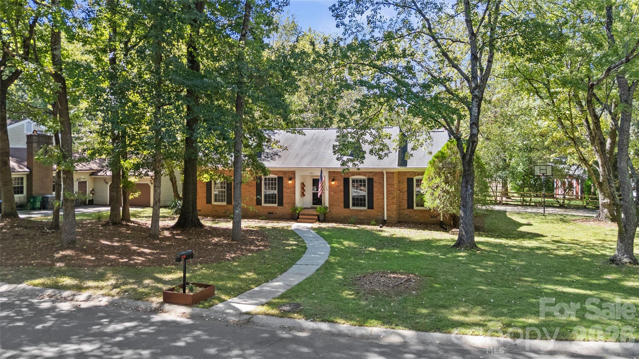 This inviting brick ranch in Sardis Forest offers updated interiors, plenty of outdoor living space, and a separate studio—all on a beautiful wooded .47-acre corner lot. The 3-bedroom, 2-bath home features 1,693 square feet with separate living and dining rooms and a comfortable family room with a wood-burning brick fireplace. Open to the family room, the refreshed kitchen includes white cabinetry, stainless appliances, a subway tile backsplash, a butcher block island, and new flooring. Nicely refurbished bathrooms, new carpet in the bedrooms, and a spacious mudroom/laundry with built-in cubbies round out the interior. The large screened porch and adjoining deck with a built-in hot tub extend the living space outdoors, with room for dining, gathering, or simply enjoying the wooded setting. The fully fenced backyard includes a detached 246-square-foot studio—ideal for a home office, exercise room, or art studio—plus a separate storage shed. Major updates include the roof in 2019, HVAC in 2022, and tankless water heater in 2023. Enjoy an established neighborhood setting with convenient access to downtown Matthews, shopping, dining, and nearby McAlpine Creek Greenway.